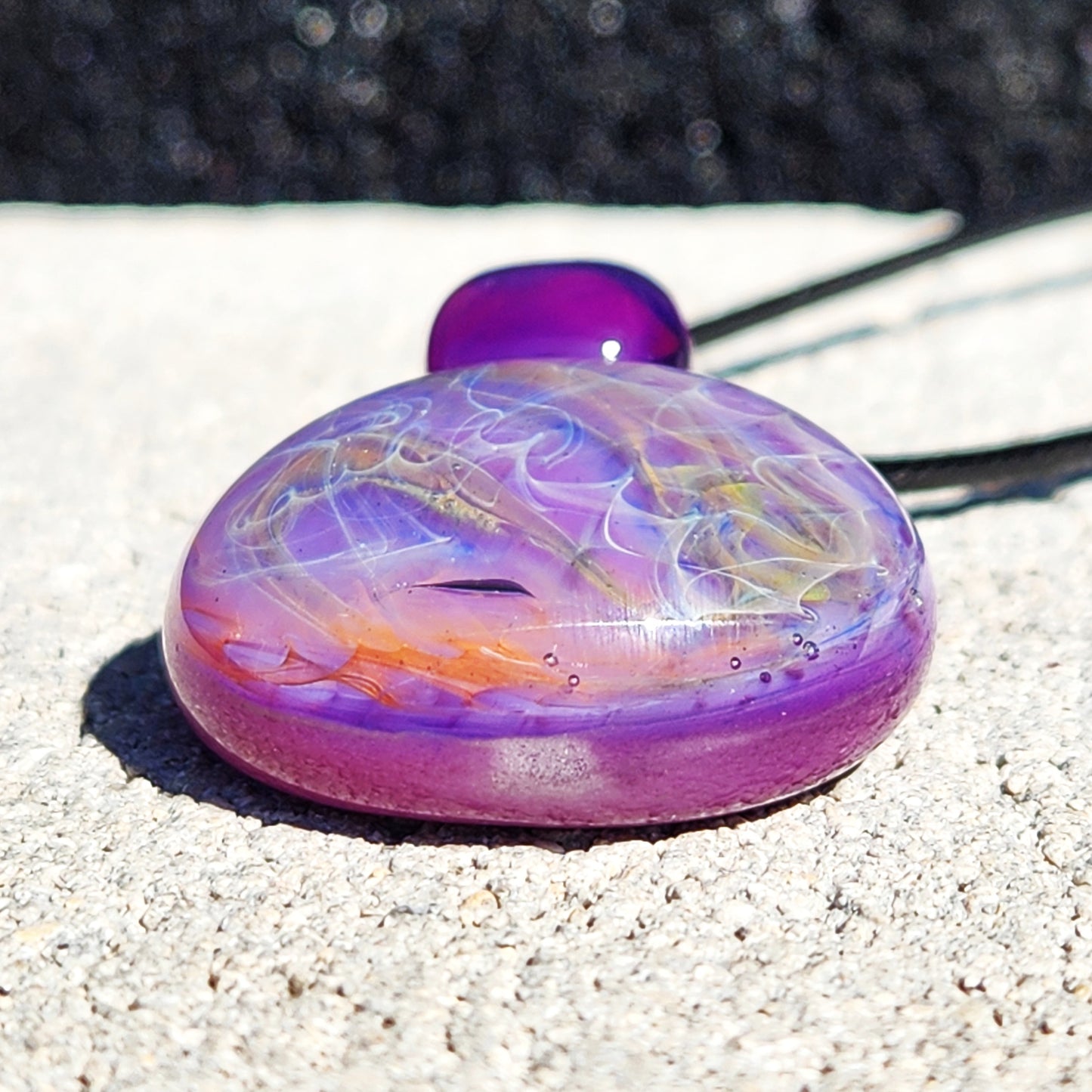Close-up of purple glass pendant necklace featuring swirling silver and gold fuming. Artisan jewelry with vibrant color and depth.