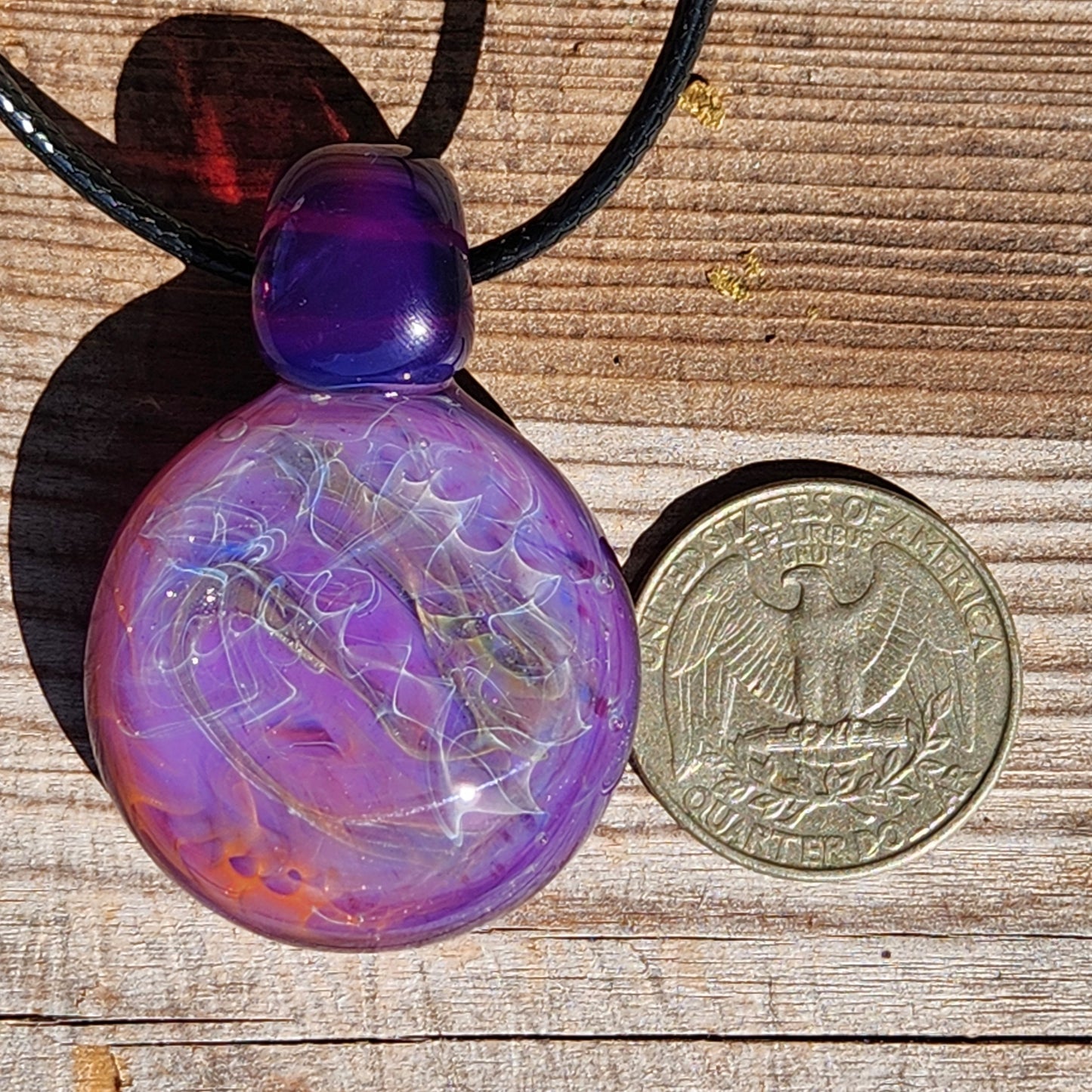 Purple glass pendant necklace next to a US quarter for size reference. Features silver and gold fuming in a bold artisan design.