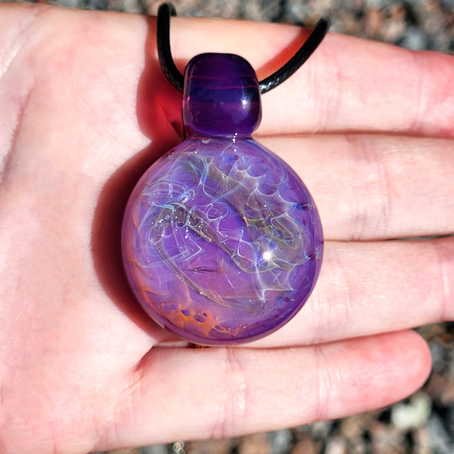 Front view of purple glass pendant necklace in hand. Silver and gold fuming create a swirling, luminous artisan jewelry piece.