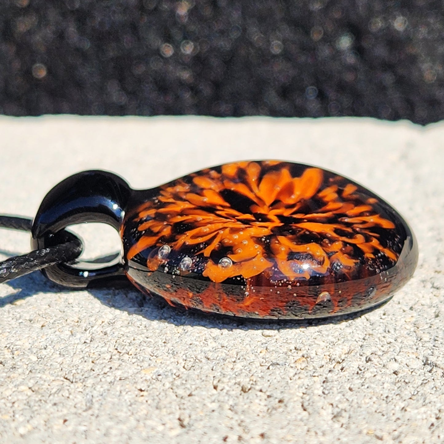 Side view of the handmade Fiery Glass Pendant Necklace showing detailed flame-like orange flower encased in glossy black glass. Unique fall accessory.
