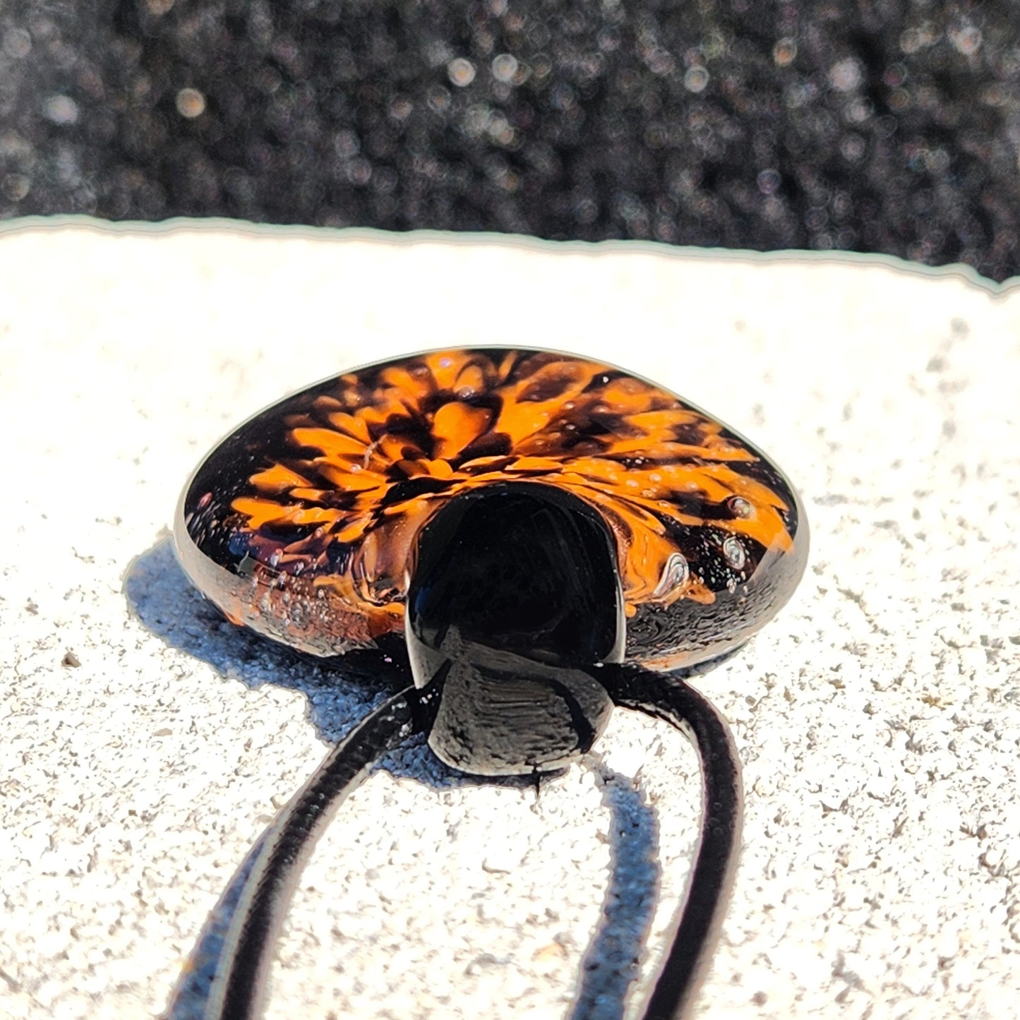 Bottom view of the Fiery Glass Pendant Necklace showing the pendant's thickness and black glass loop. Artisan fall jewelry with fiery floral design.