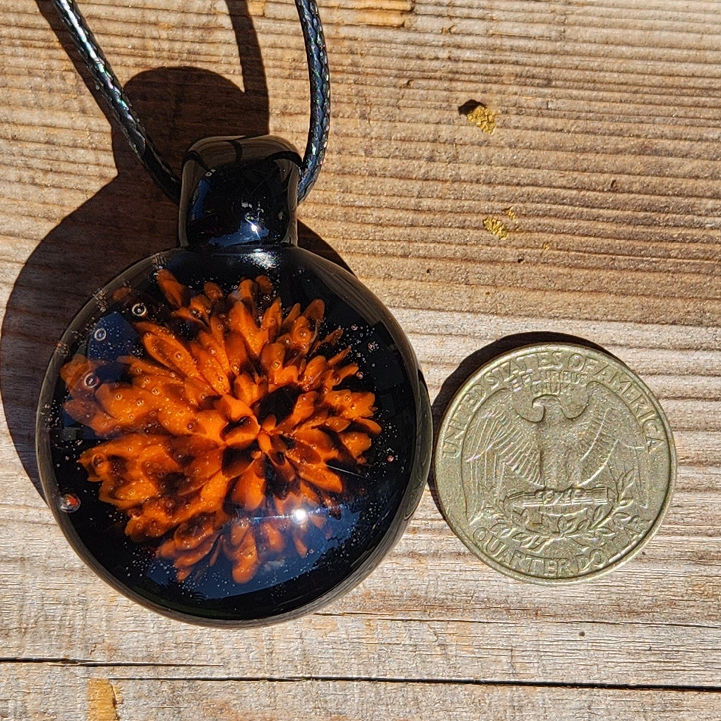Fiery Glass Pendant Necklace next to a US quarter for size comparison. Handmade Halloween-inspired jewelry with bold orange and black glass detail.