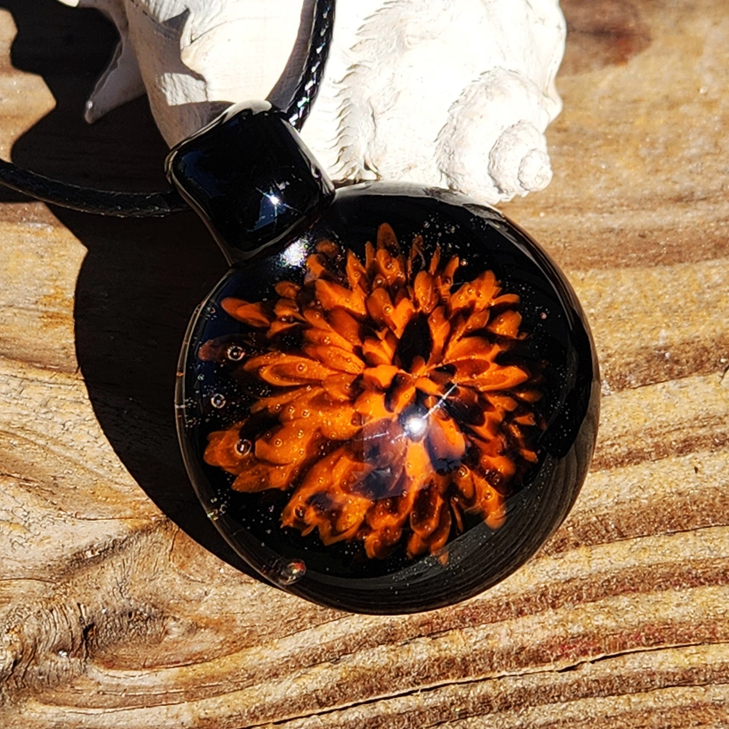 Fiery Glass Pendant Necklace displayed on wood with sunlight enhancing the orange and red bloom. Unique handmade Halloween-inspired jewelry piece.