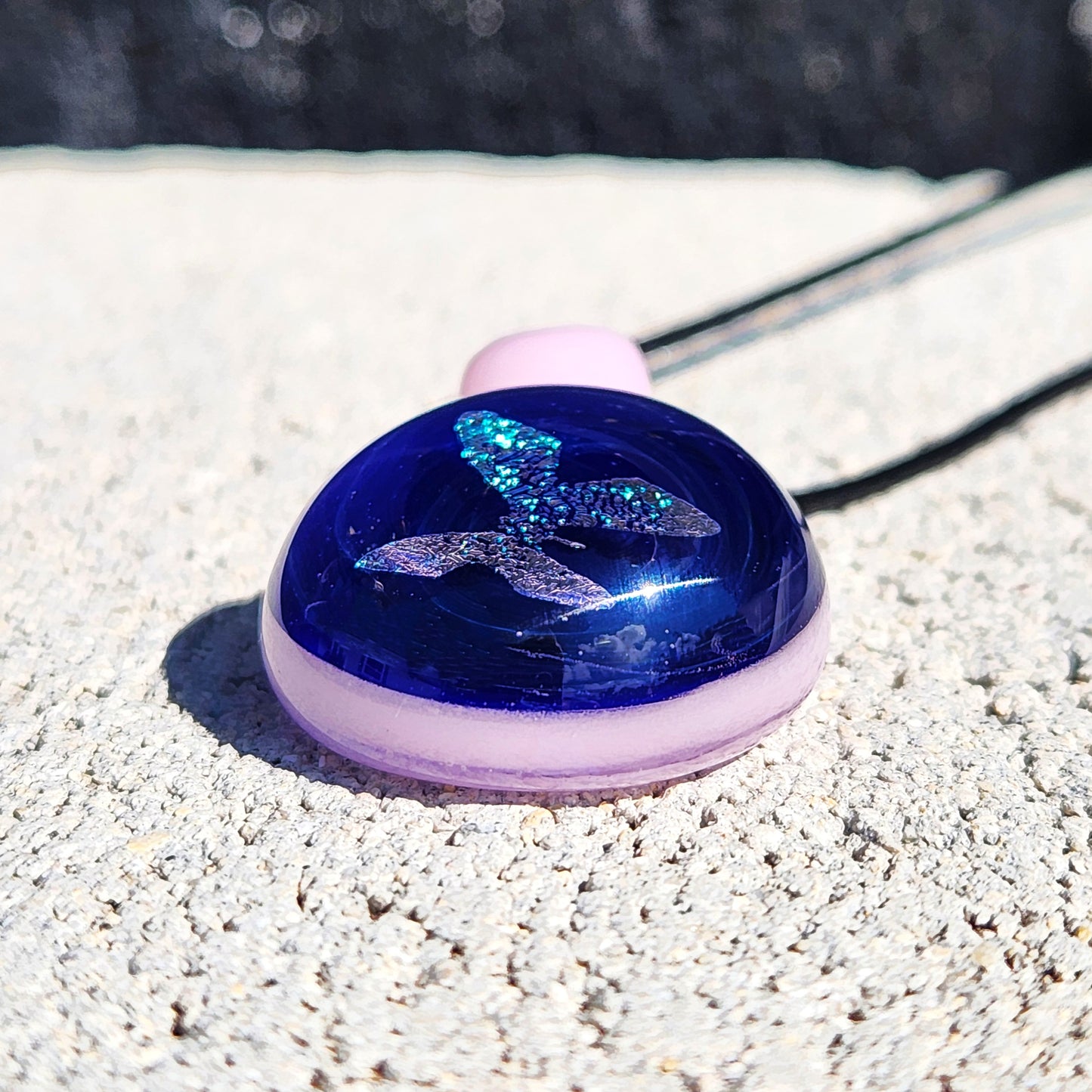 Side view of small glass butterfly pendant showing domed blue surface and pink loop, ideal for delicate jewelry lovers.