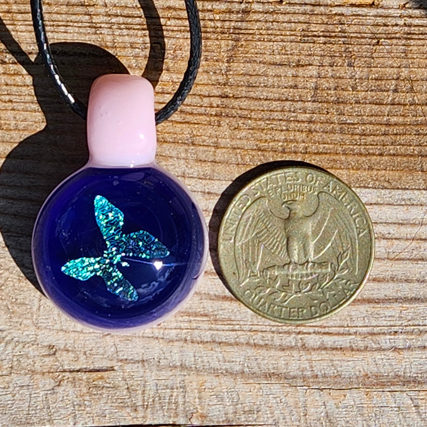 Size comparison of small butterfly pendant next to a US quarter, showing compact handmade design with blue and pink glass.