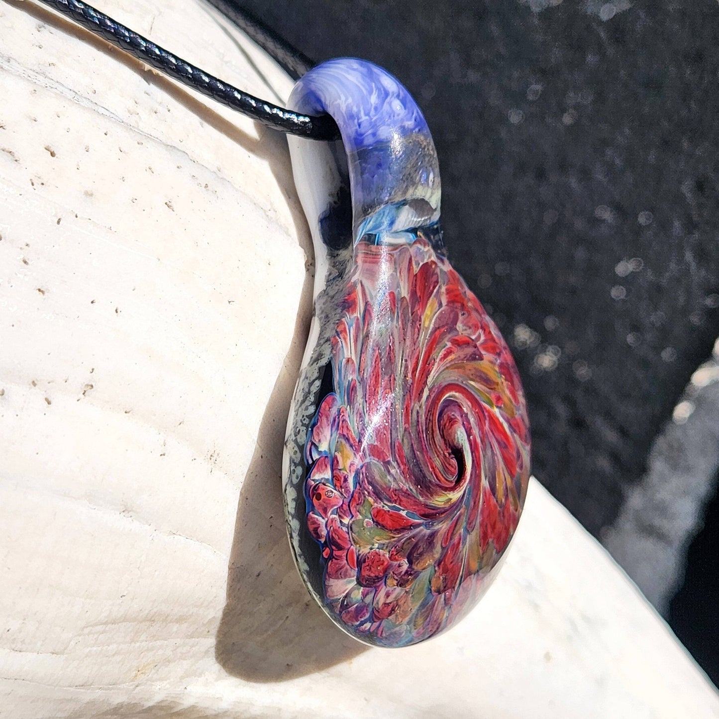 Close-up of handmade heady glass pendant necklace showing intricate red and amber swirl pattern. Artistic handblown glass gift for jewelry lovers.