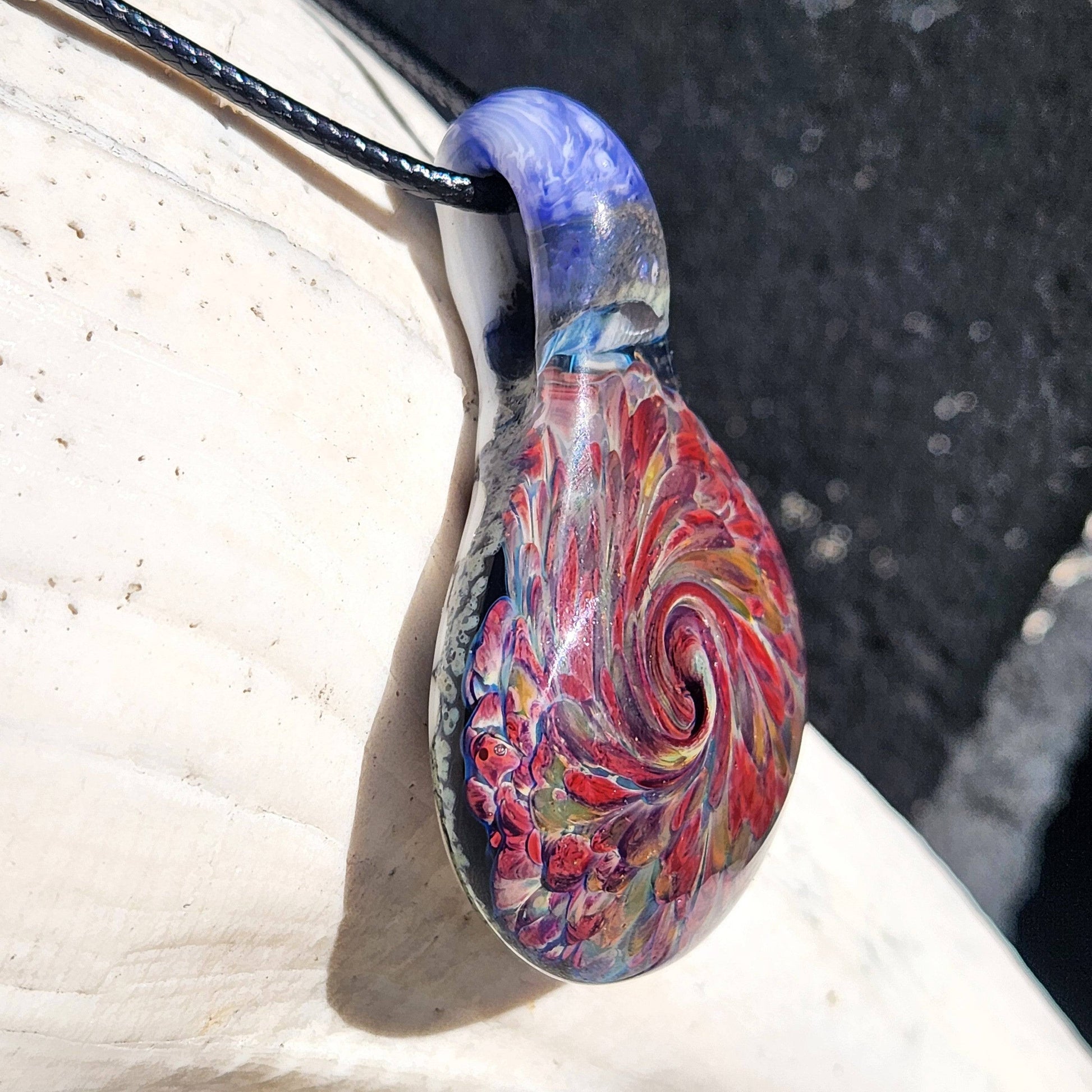 Close-up of handmade heady glass pendant necklace showing intricate red and amber swirl pattern. Artistic handblown glass gift for jewelry lovers.