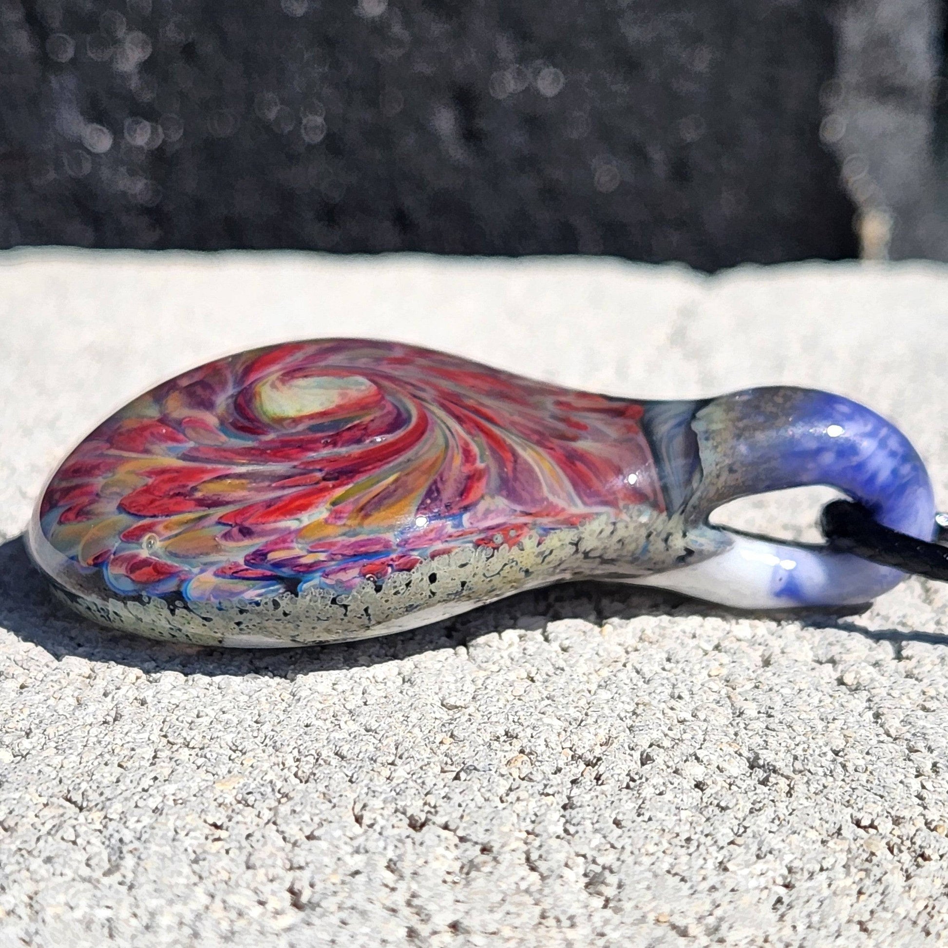 Detailed side profile of handmade glass pendant necklace with red and amber swirl. Handblown borosilicate glass jewelry for statement wear.