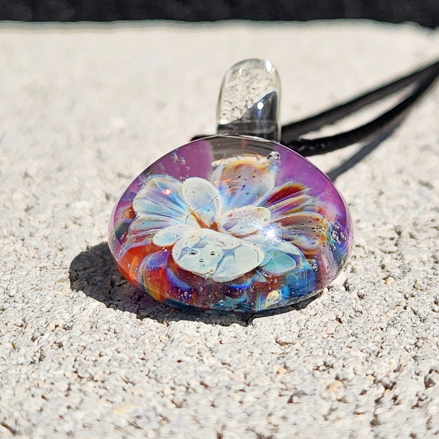 Handmade Glass Pendant resting on stone surface, showcasing intricate blue and purple bloom with UV-reactive colors.