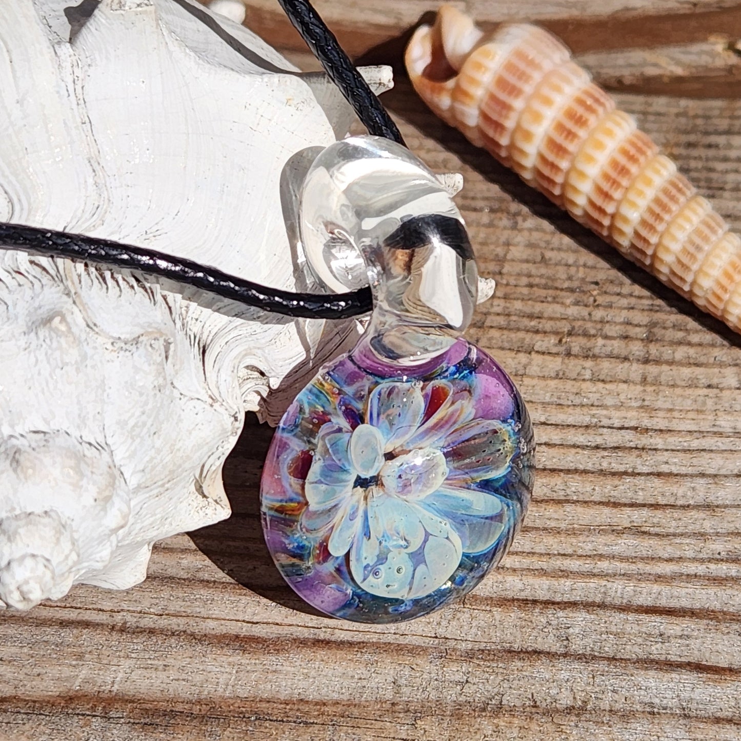 Handmade Glass Pendant displayed on wood with seashells, showing detailed blue and purple bloom and clear loop.