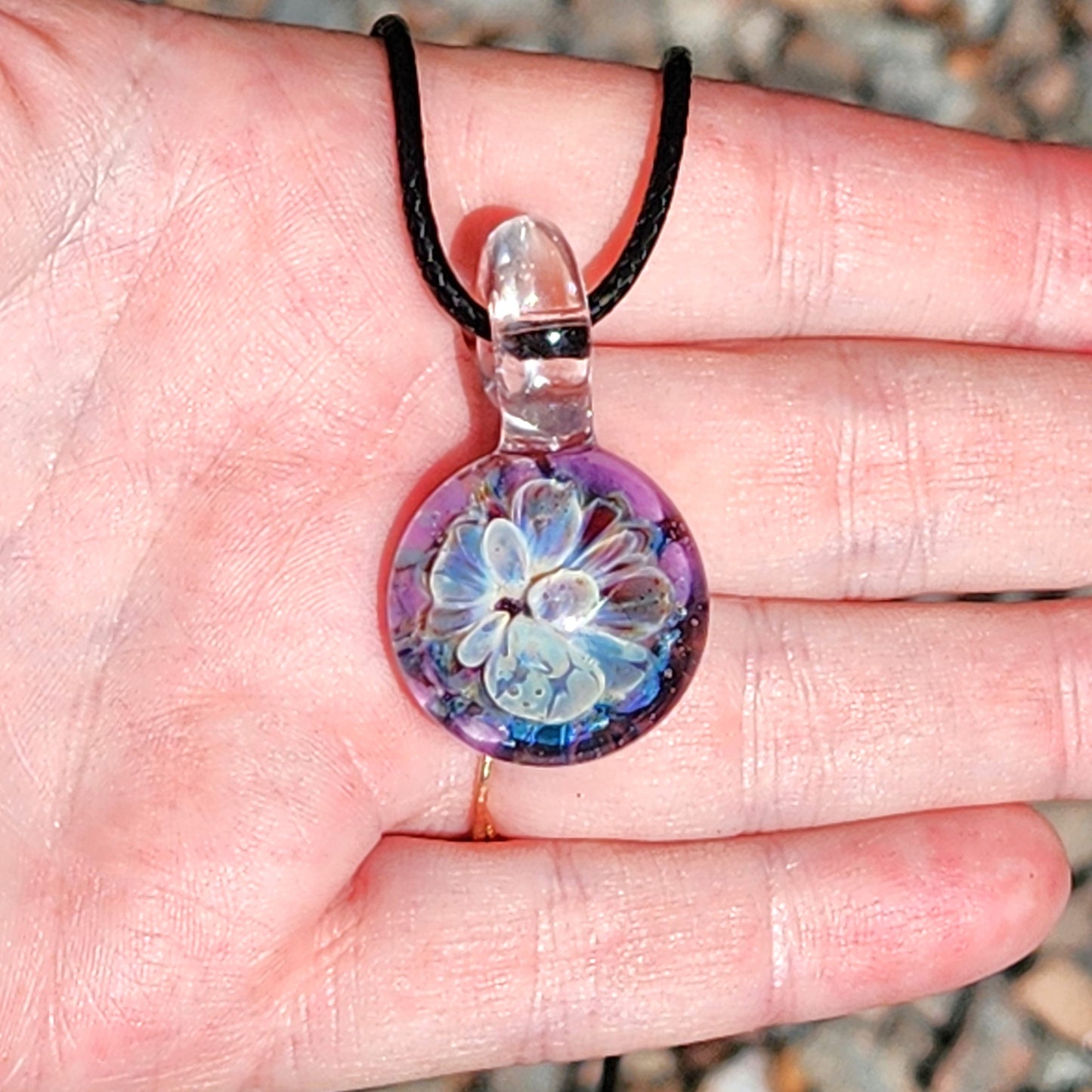 Hand holding Handmade Glass Pendant with blue and purple bloom, showing size and detail of UV-reactive jewelry piece.