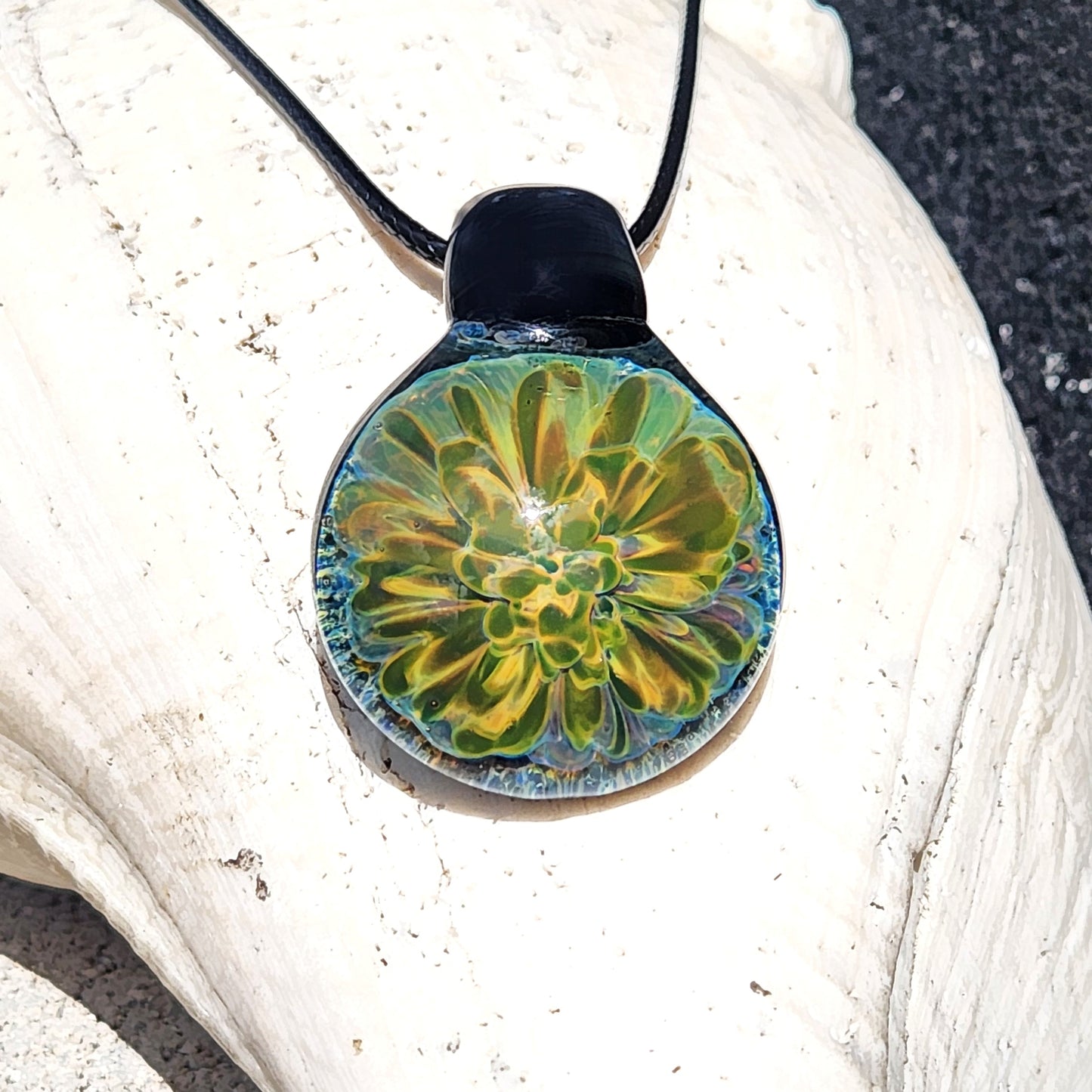 Handmade glass pendant with glowing yellow-green floral design on black cord, displayed on a white seashell. Unique jewelry gift in gift box.