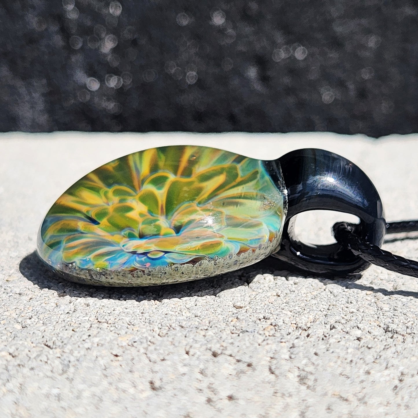 Angled view of handmade borosilicate pendant with glowing yellow-green design. Part of handmade glass jewelry collection.