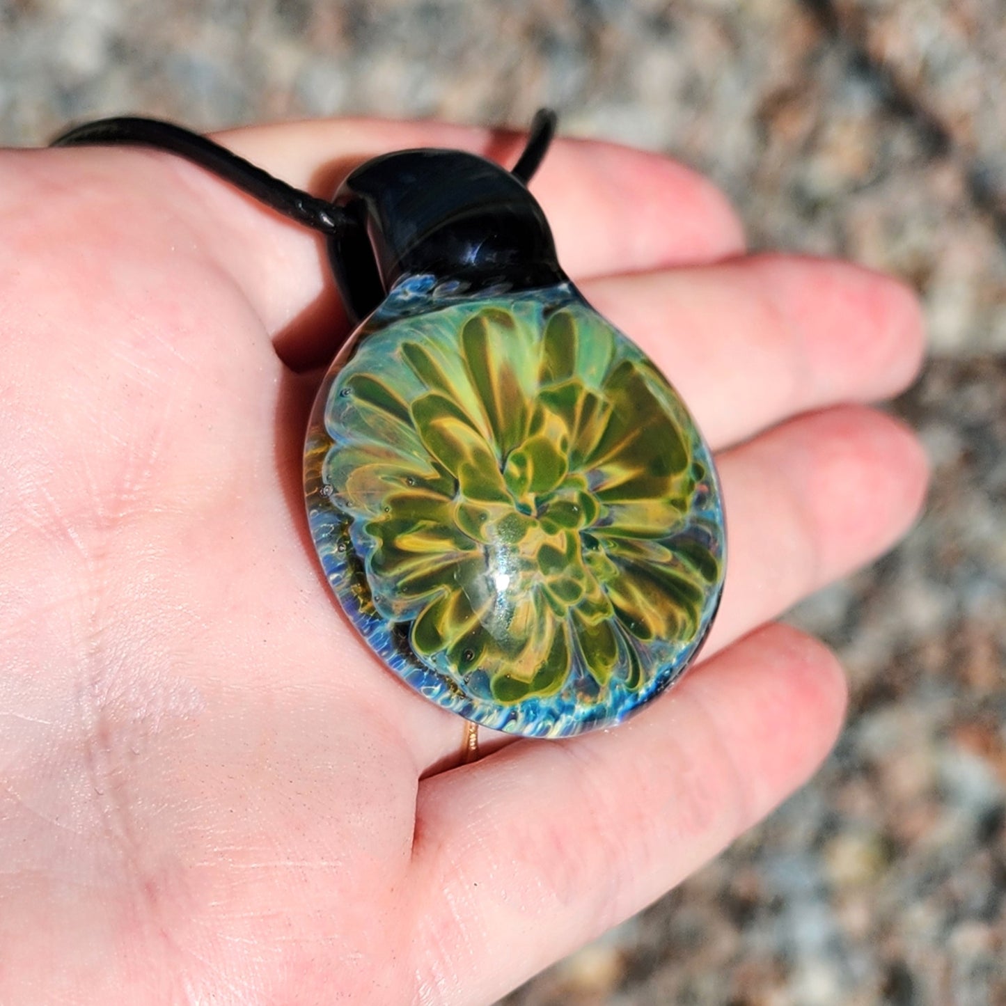 Hand holding handmade glass pendant with glowing yellow-green floral design. Unique borosilicate necklace in jewelry gift category.