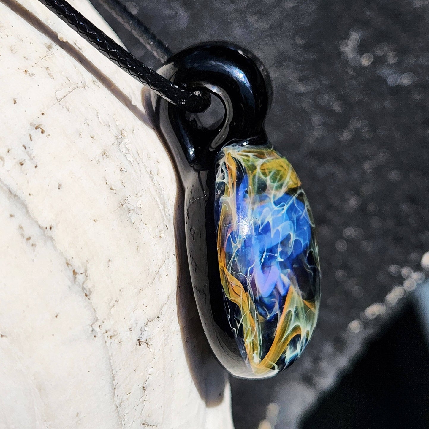 Side view of handmade glass pendant featuring vibrant blue, gold, and silver swirls on a black base, ideal for cosmic-themed jewelry collections.