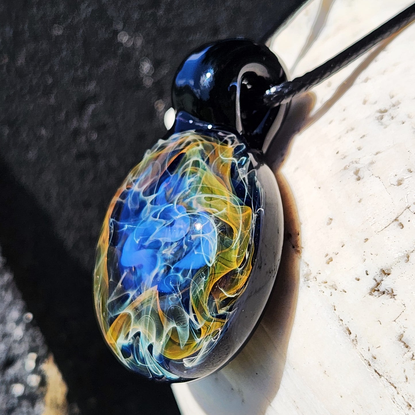 Angled view of cosmic glass pendant necklace with gold, orange, and blue swirls, highlighting its handcrafted celestial design.