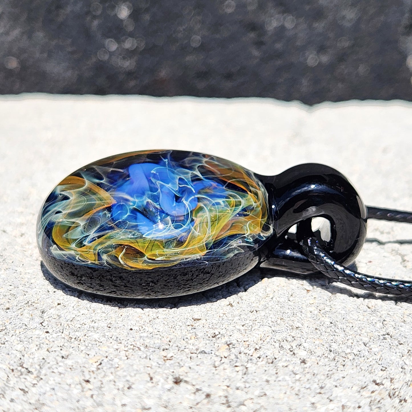 Side profile of cosmic glass pendant necklace with vibrant gold and blue swirls, handcrafted for celestial jewelry enthusiasts.