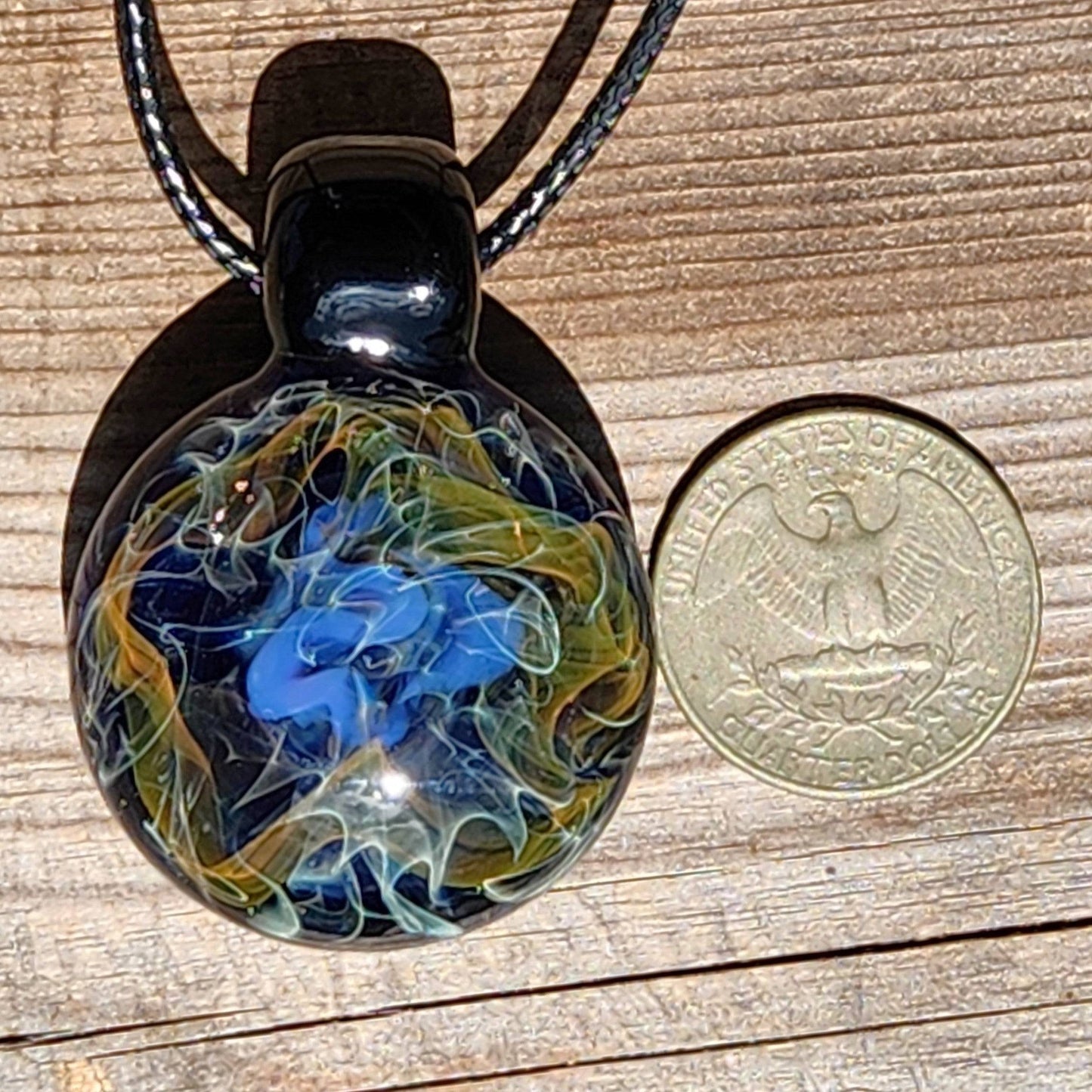 Size comparison of handmade glass pendant with a U.S. quarter, showing detailed gold and blue cosmic swirls on a black background.