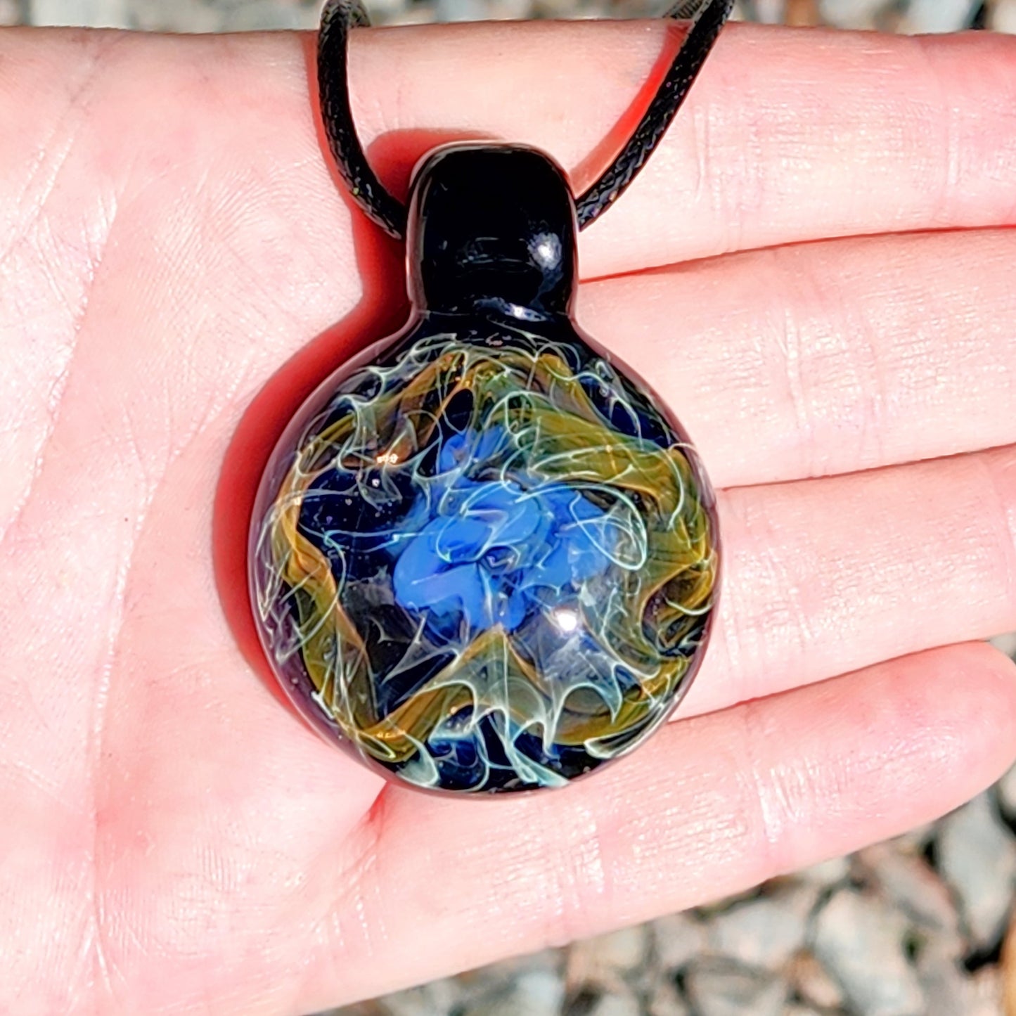 Handheld view of gold and silver fumed glass pendant necklace, displaying vibrant cosmic swirl design in blue, gold, and white tones.