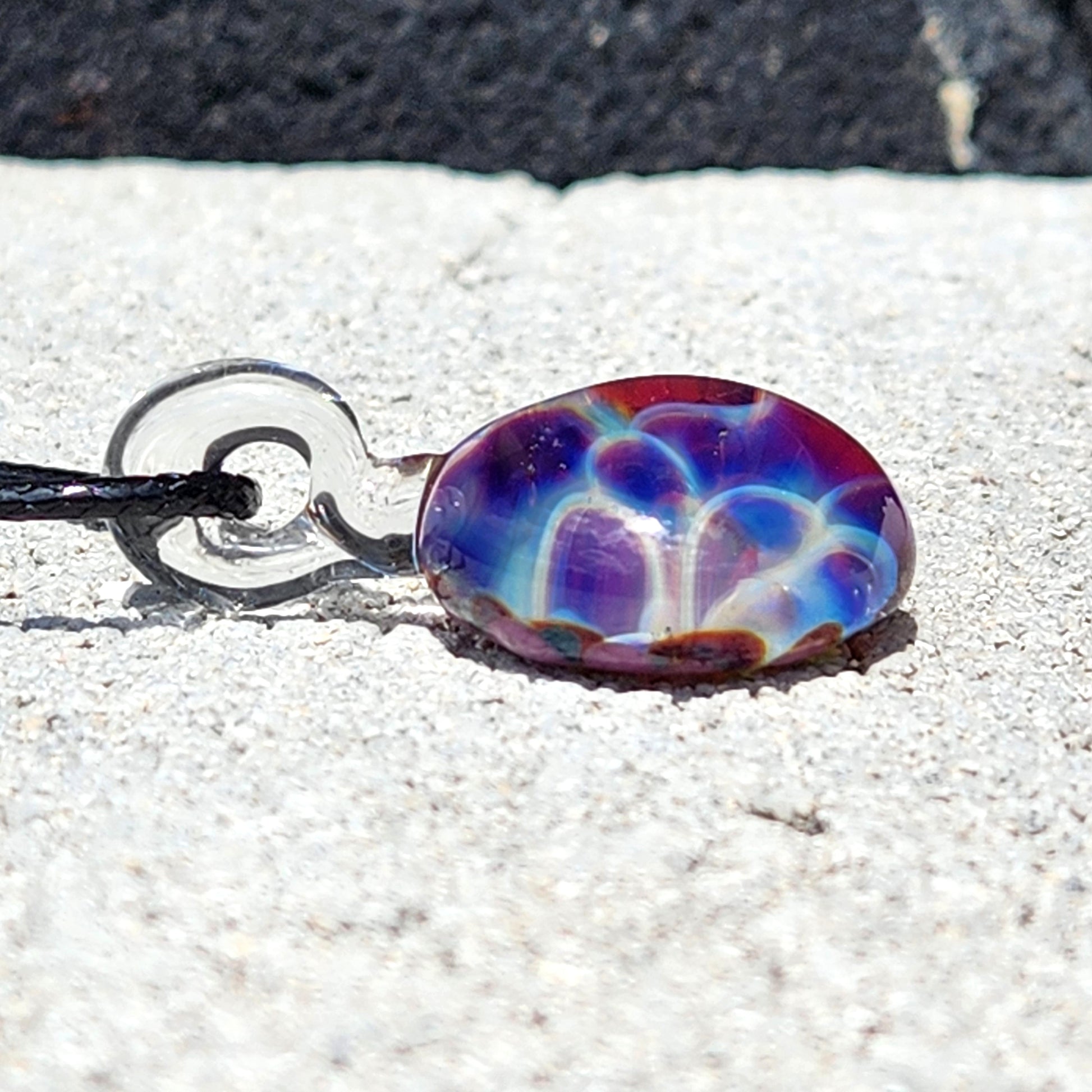 Detailed side angle of handmade rainbow bubble dot pendant in purple and blue tones, suspended on black cord for wearable art style.