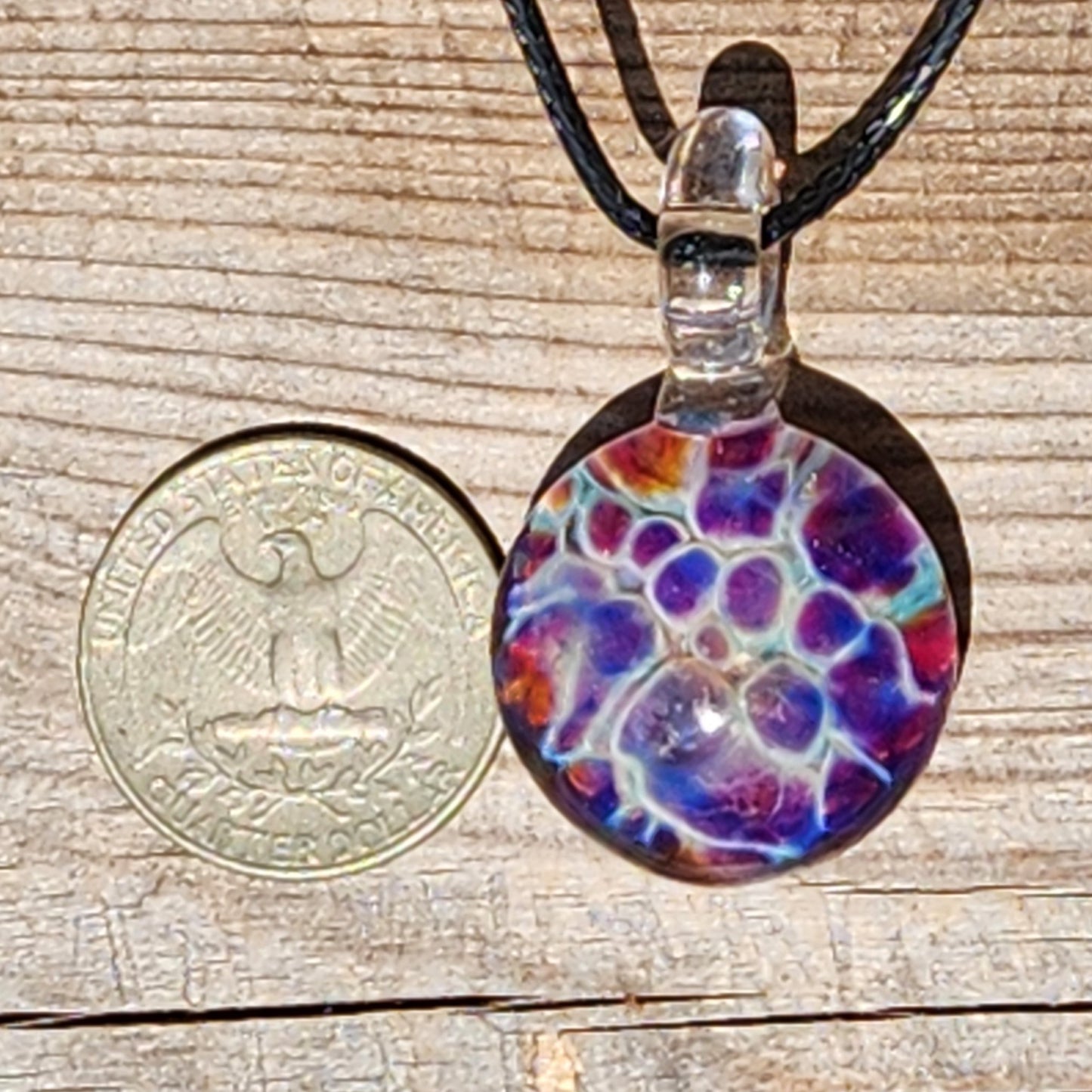 Handmade glass pendant with purple and blue bubble design shown next to US quarter for size comparison, ideal for charm jewelry shoppers.
