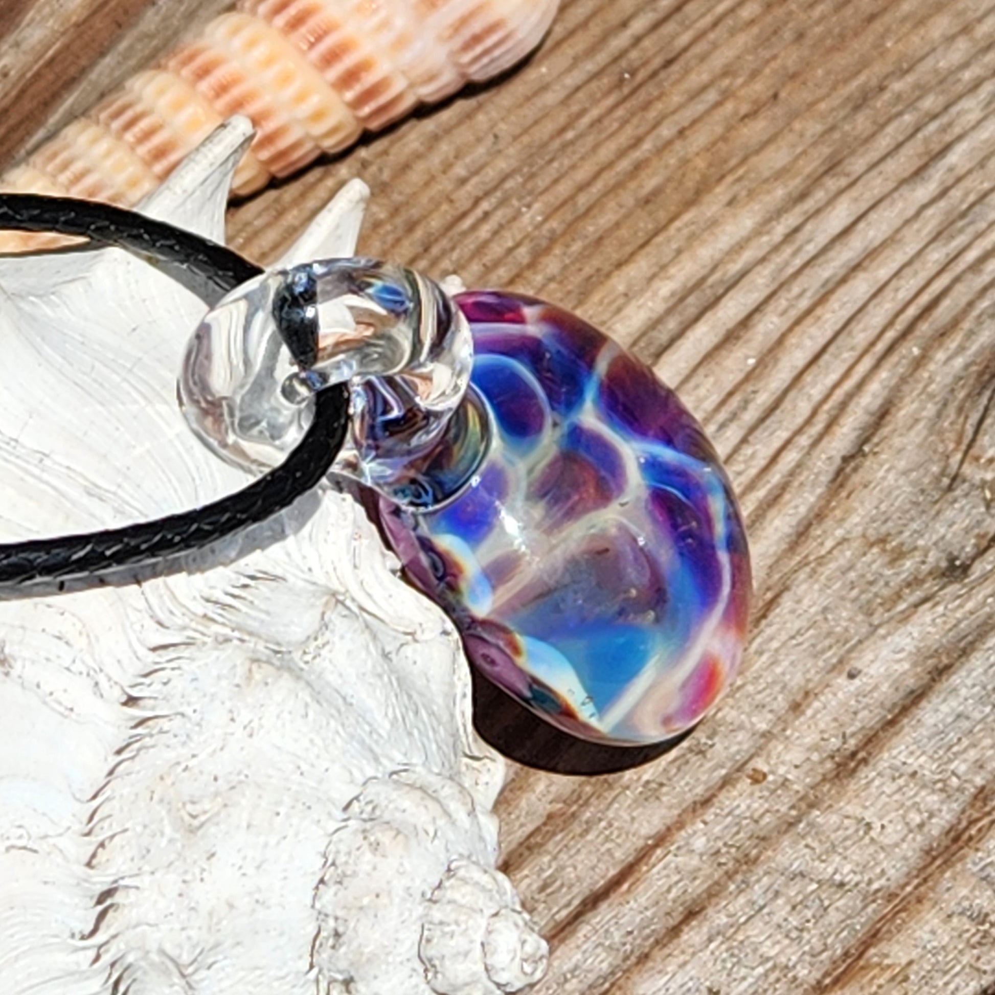 Artistic borosilicate glass pendant with rainbow bubble pattern in purple and blue, displayed on rustic wood with seashells.