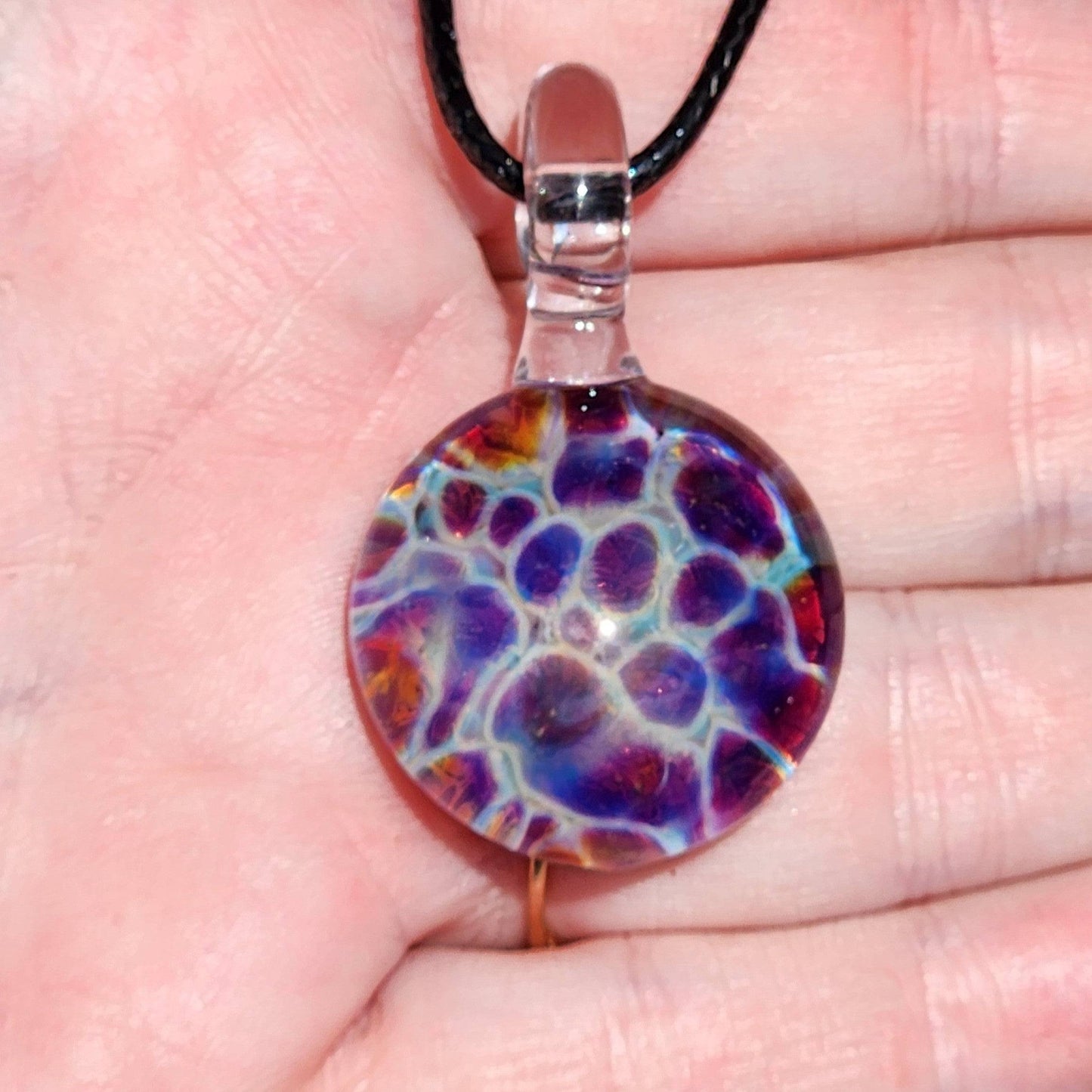 Handheld view of handmade glass pendant with vibrant purple, blue, and red hues in bubble dot design, perfect for gifting.