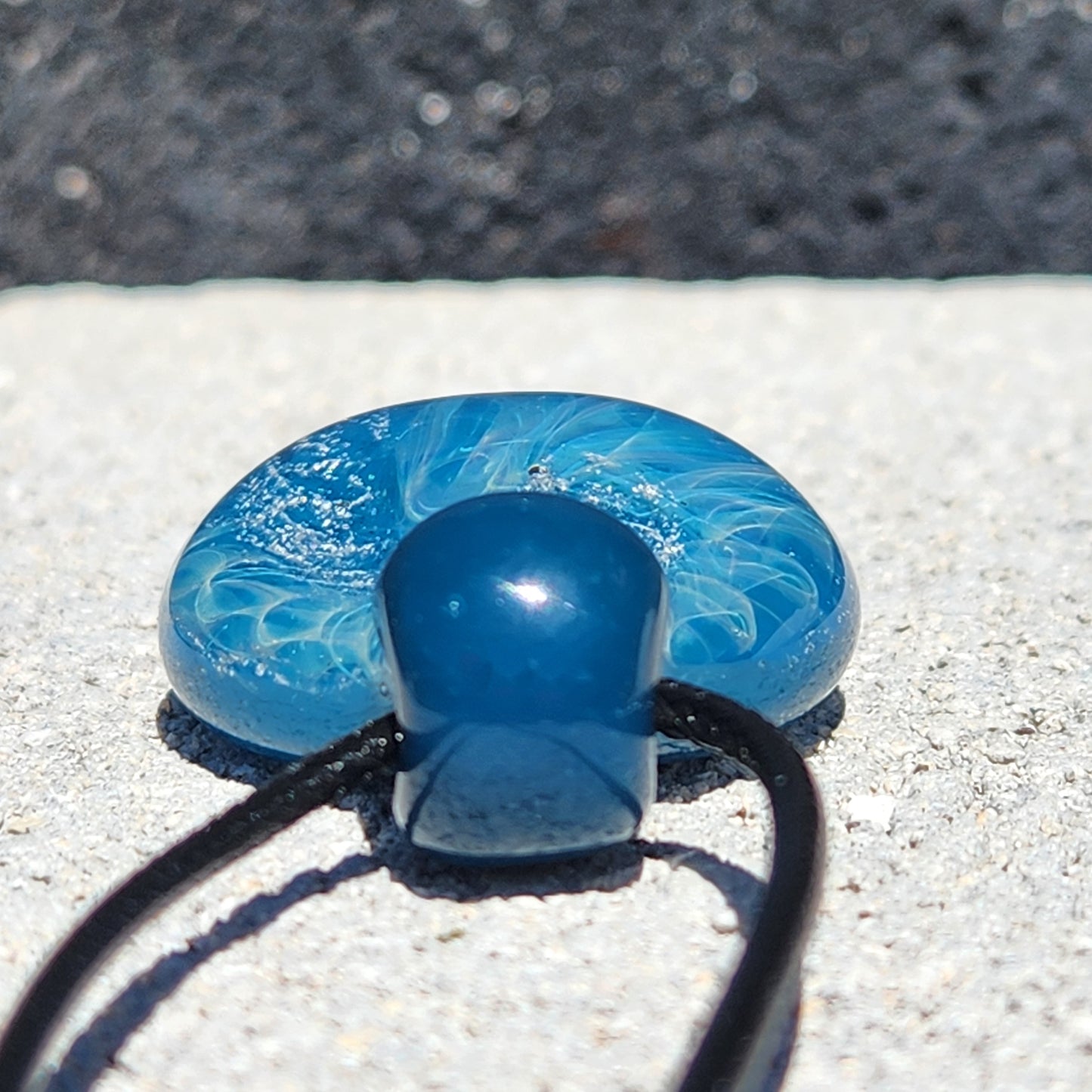 Bottom view of handmade glass pendant necklace showing smooth blue glass loop and swirling ocean pattern.