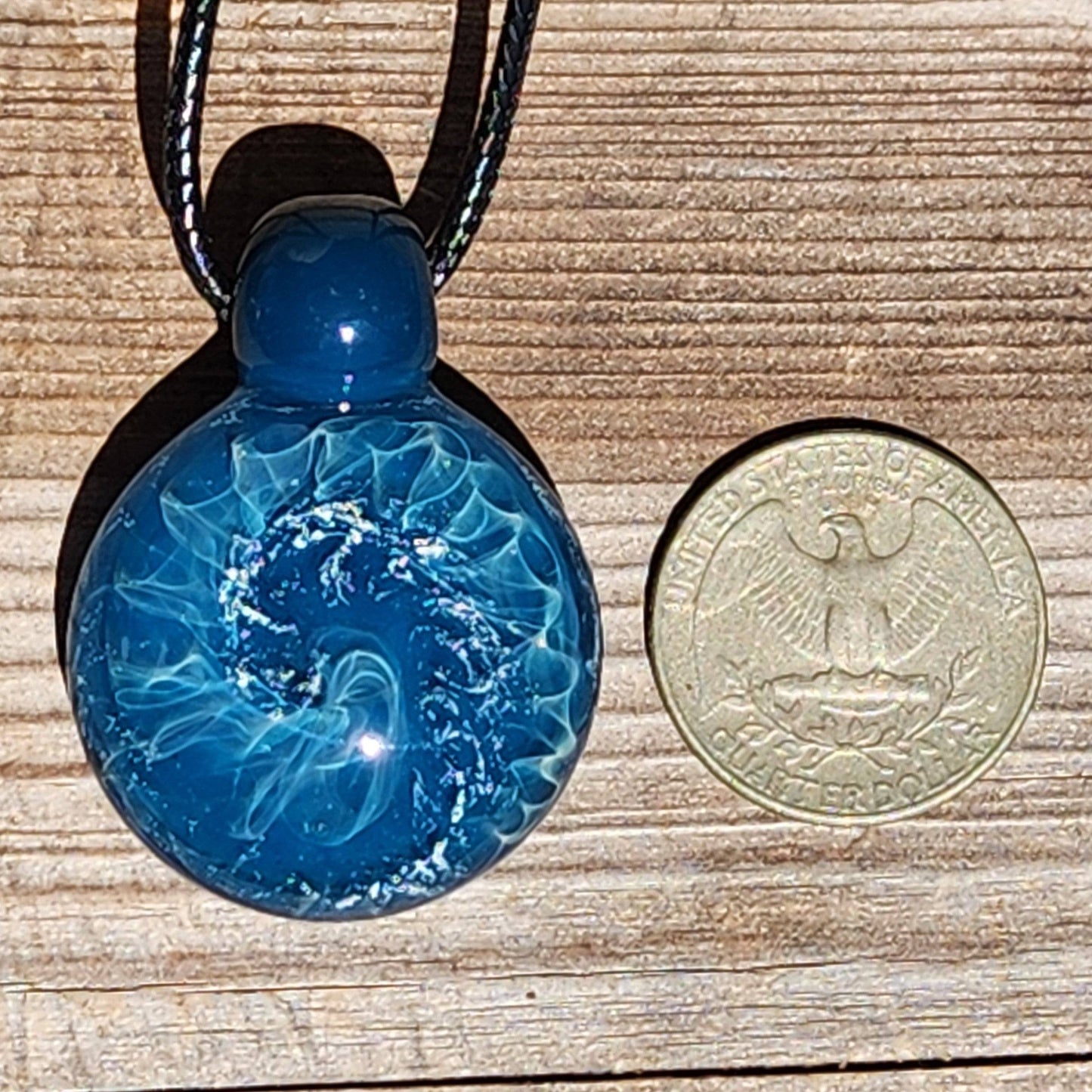 Size comparison of ocean-inspired glass pendant next to a U.S. quarter, showing detailed wave design and silver shimmer.