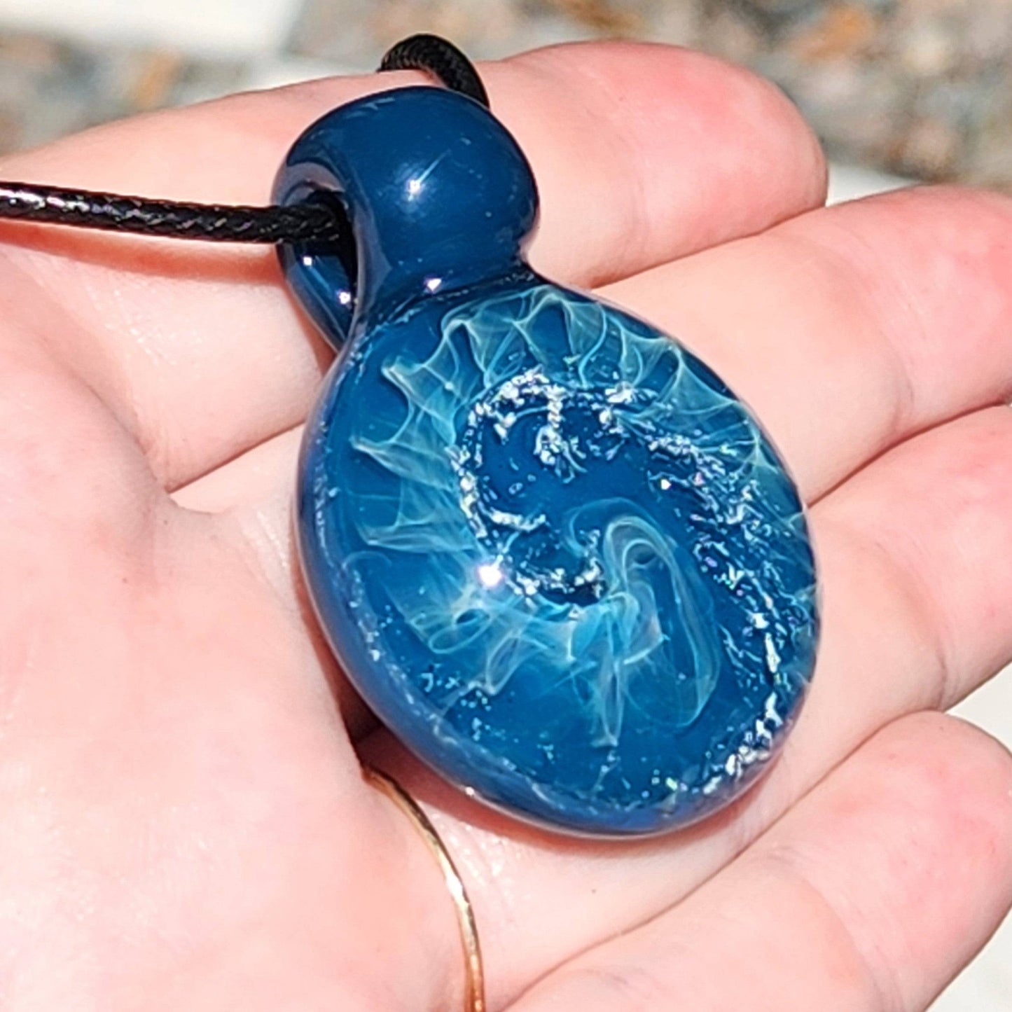 Handheld view of handmade blown glass pendant with ocean swirl and silver accents, showing size and glossy finish.