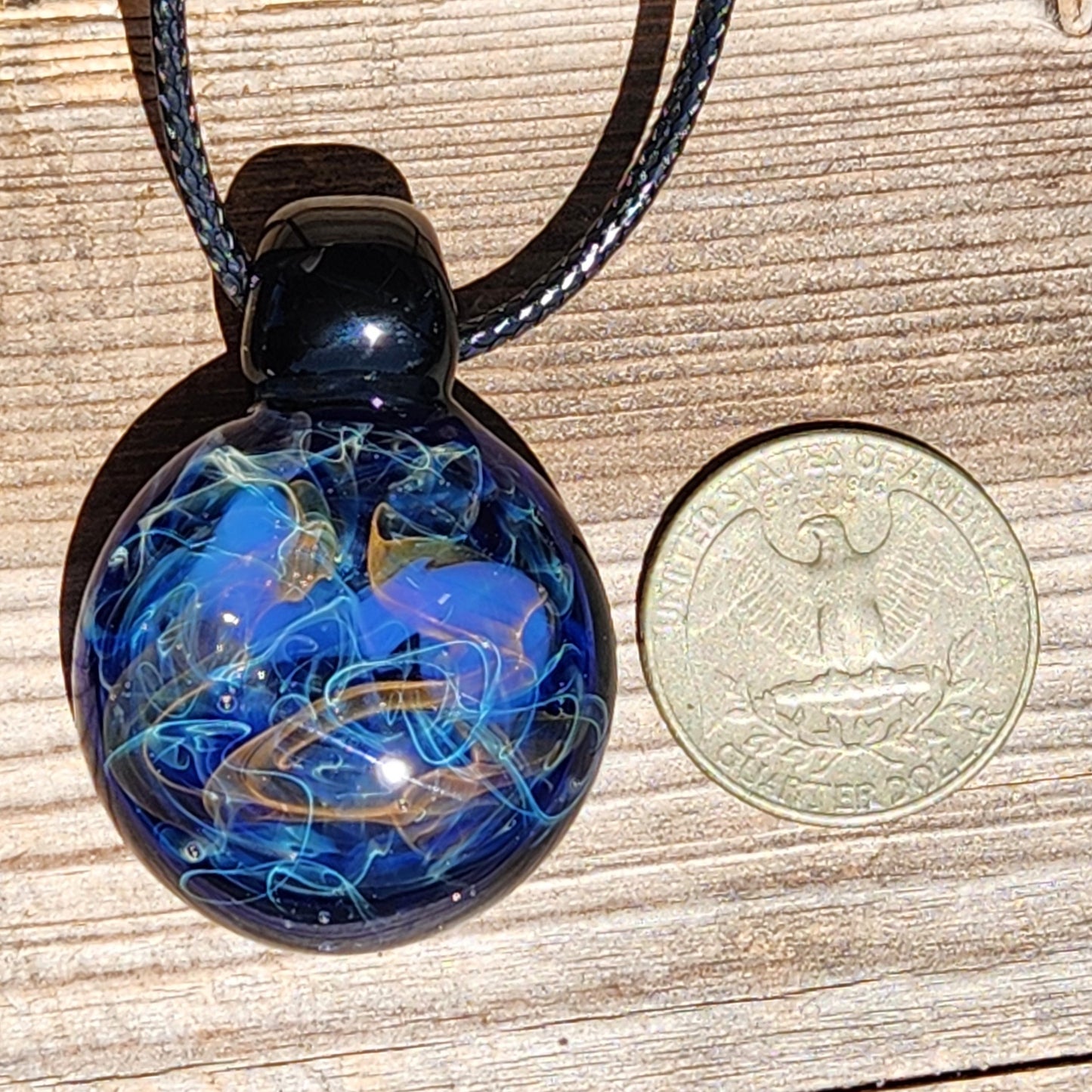 Handmade Glass Pendant – Unique Gold & Silver Fumed Black Necklace next to US quarter for size comparison on wood surface.