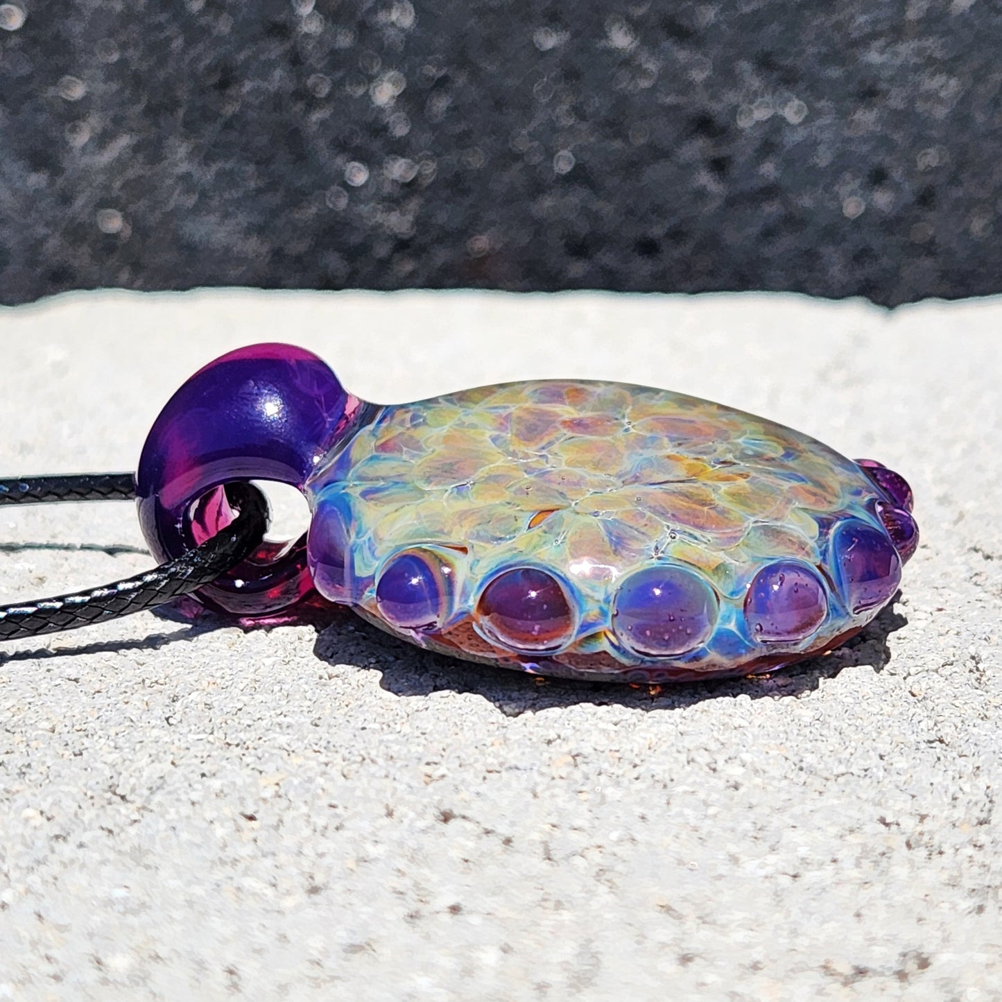 Low angle of handmade borosilicate pendant showing domed glass surface and purple bubble detailing. Unique glass jewelry gift idea.