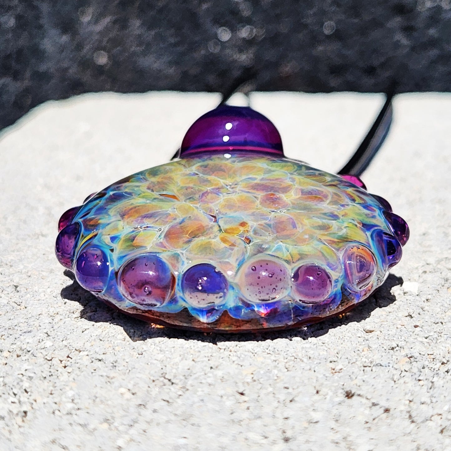 Bottom view of handmade rainbow shimmer pendant with textured purple glass edge. Artistic borosilicate jewelry for bold fashion.