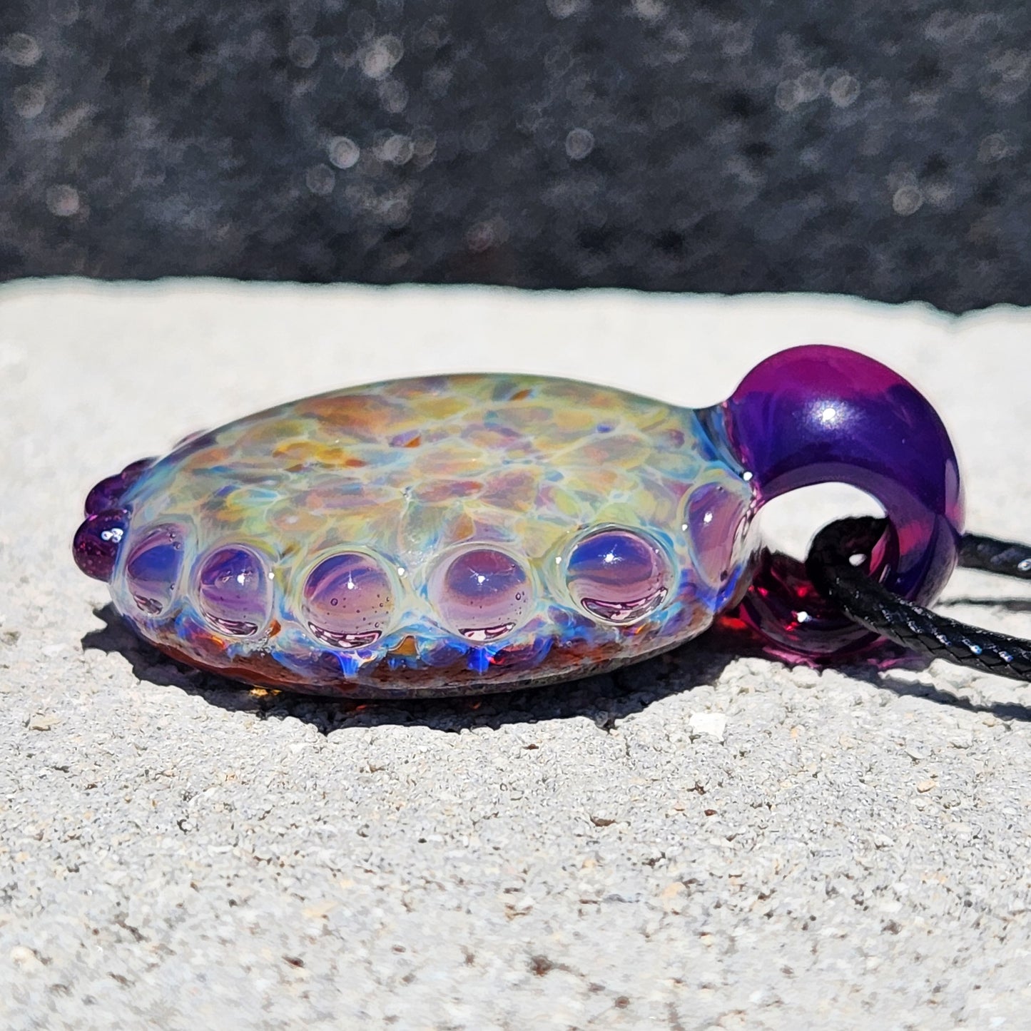 Side profile of handmade glass pendant necklace with multicolor shimmer and purple loop bail. Unique borosilicate jewelry gift.