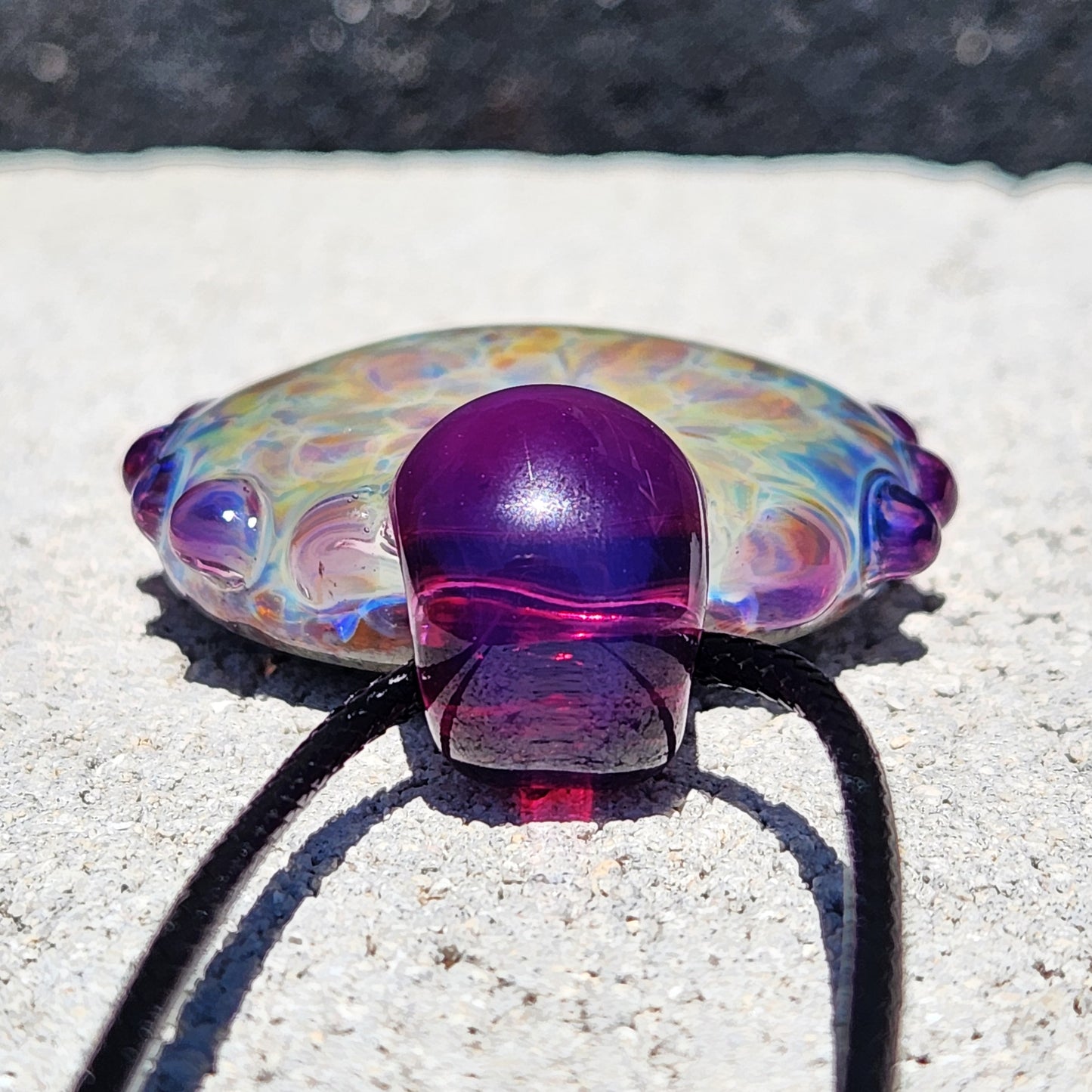 Top view of handmade borosilicate pendant showing purple glass loop and vibrant shimmer. Artistic glass jewelry gift necklace.
