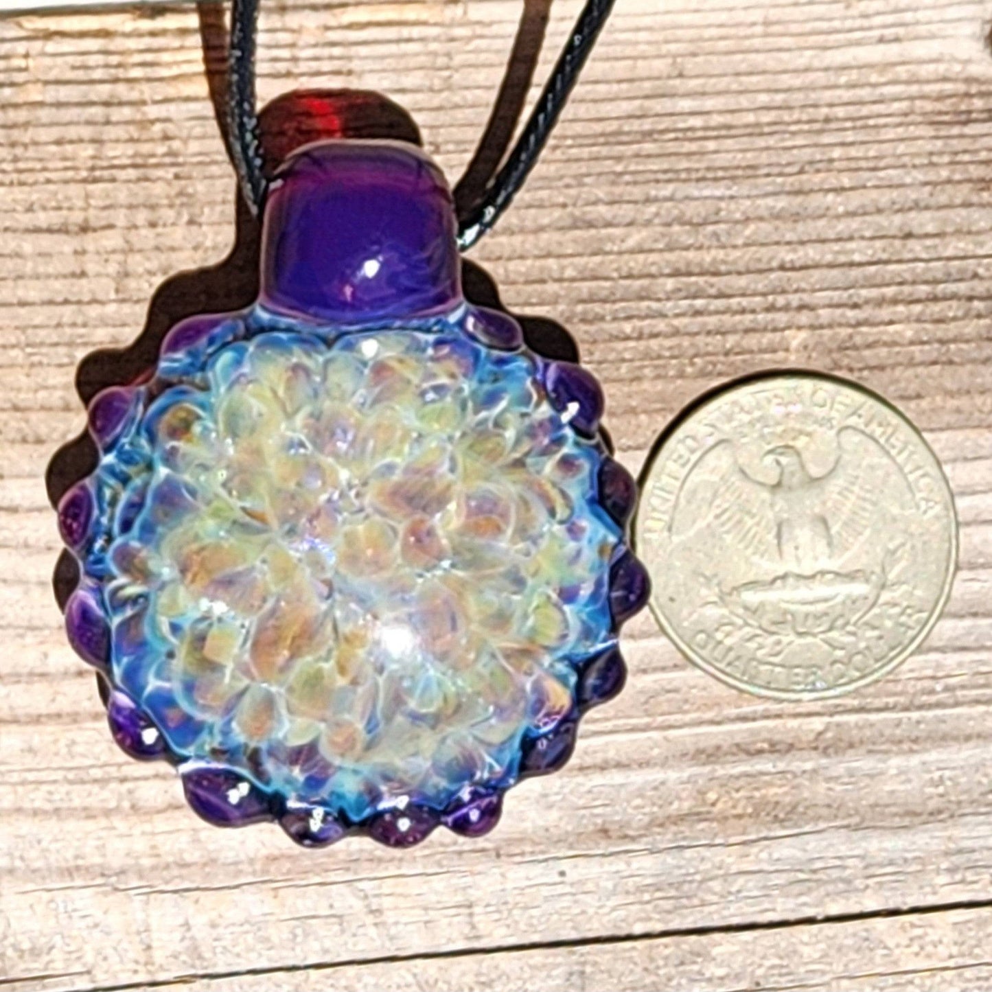 Handmade glass pendant next to a U.S. quarter for size comparison, featuring rainbow shimmer and purple accents. Large borosilicate necklace gift.