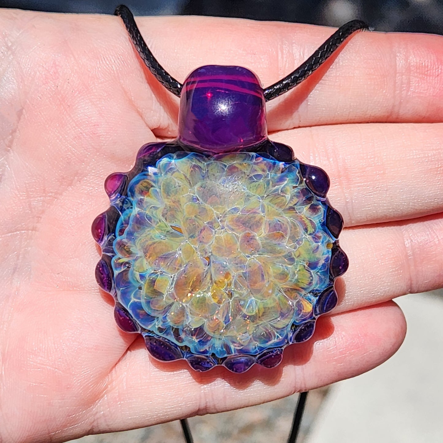 Hand holding handmade glass pendant with rainbow shimmer and purple edge, showing size and detail. Large borosilicate statement necklace.