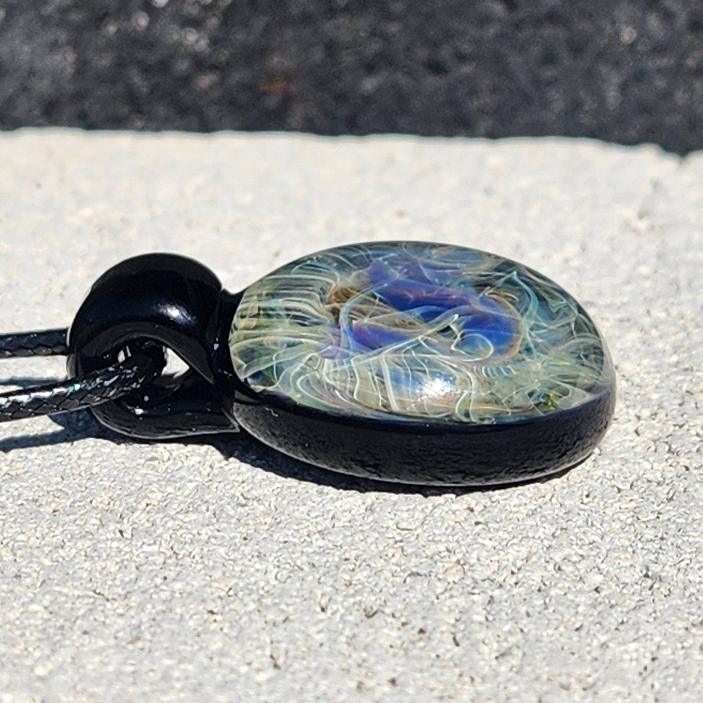 Flat angle of blown glass pendant with black base and vibrant swirling colors. Unique handmade necklace with space-inspired design.