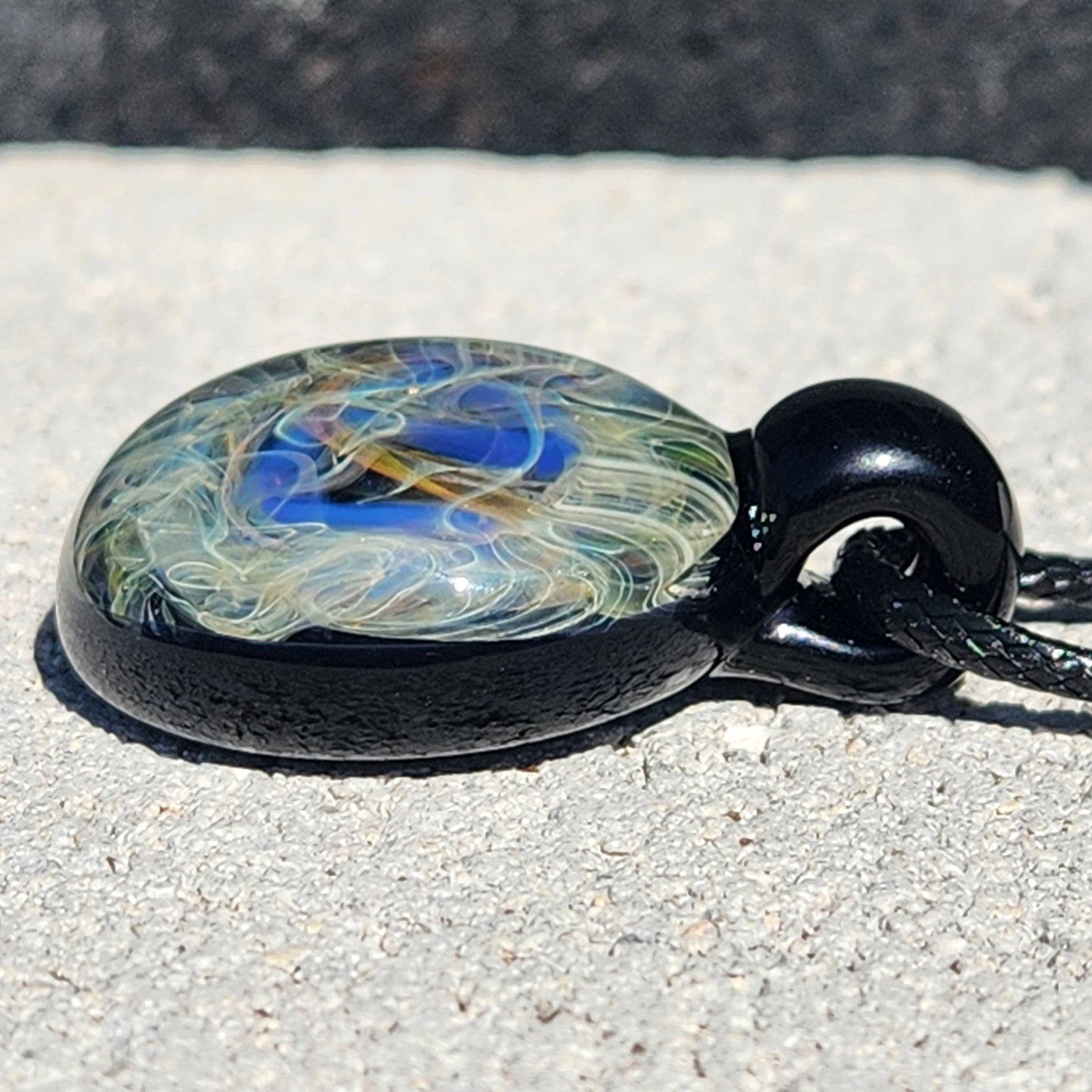 Side profile of handmade glass pendant showing depth of swirling blue and gold design. Unique blown glass jewelry with cosmic theme.