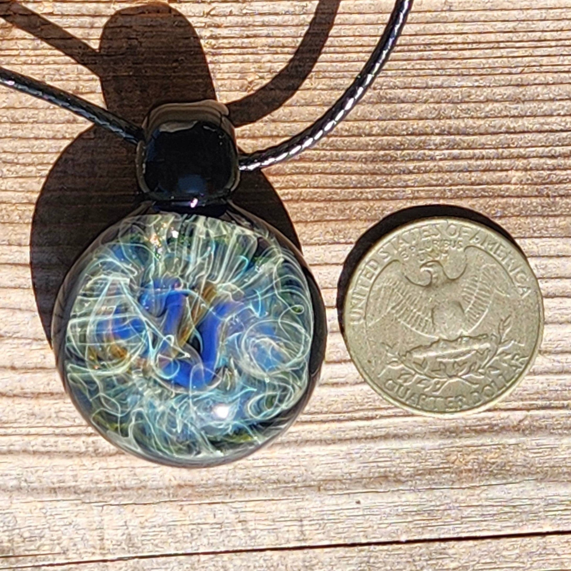 Size comparison of handmade glass pendant necklace next to US quarter. Unique heady glass jewelry with swirling cosmic design.