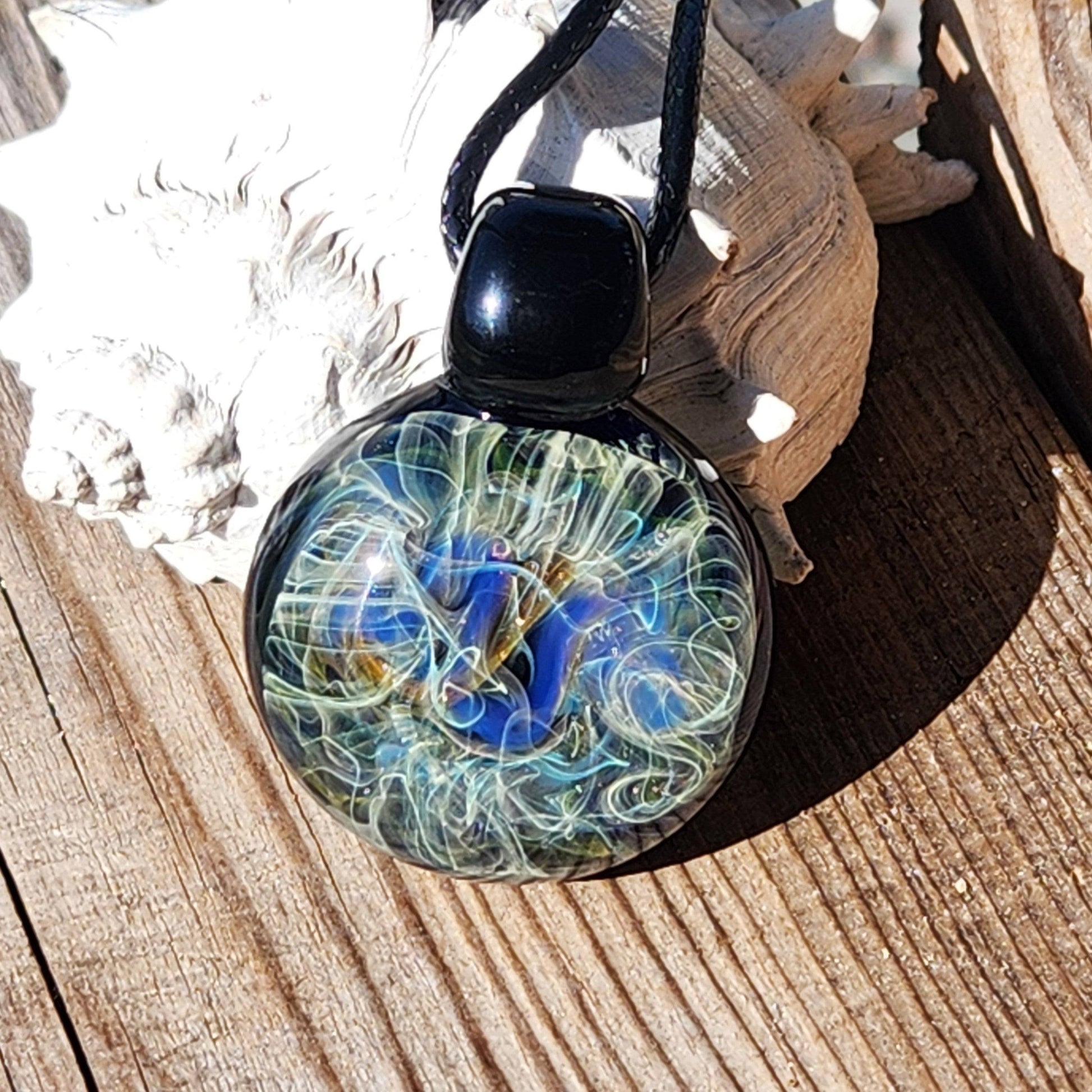 Heady glass pendant necklace with cosmic swirls of blue, gold, and silver, displayed on wood. Handmade jewelry with artistic flair.