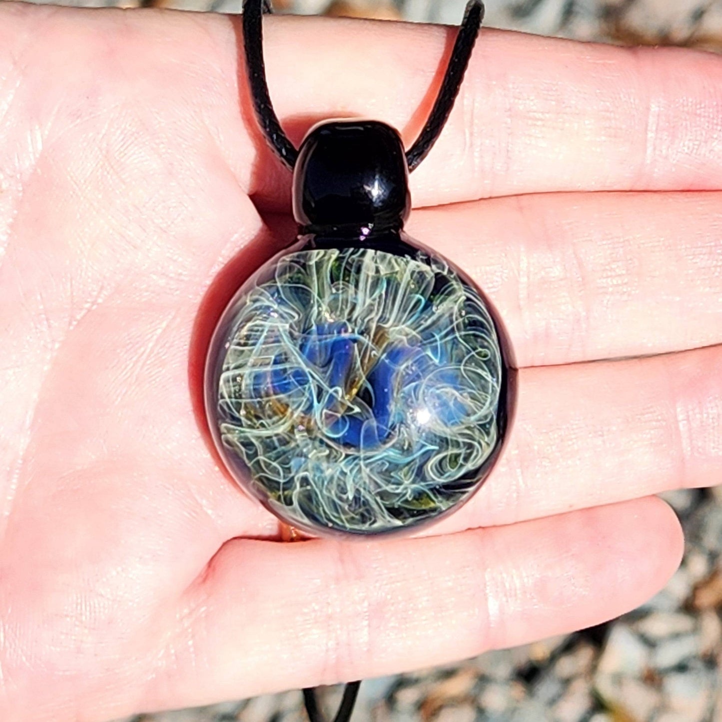 Hand holding handmade glass pendant necklace with swirling blue and gold design. Unique heady glass jewelry made in the USA.