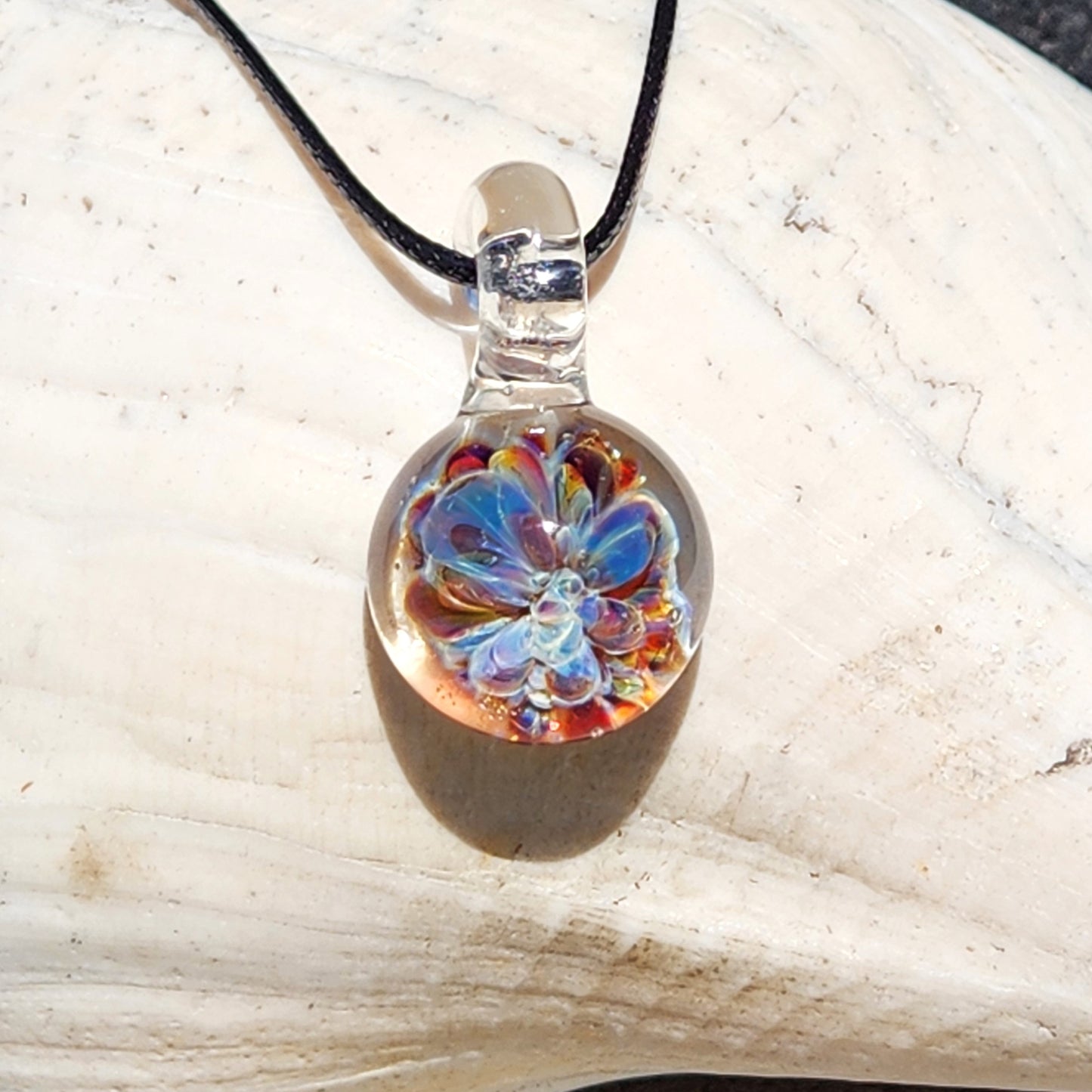 Handmade UV Glow Glass Pendant with multicolor flower encased in clear glass, displayed on a shell. Lightweight necklace for gifts or festivals.