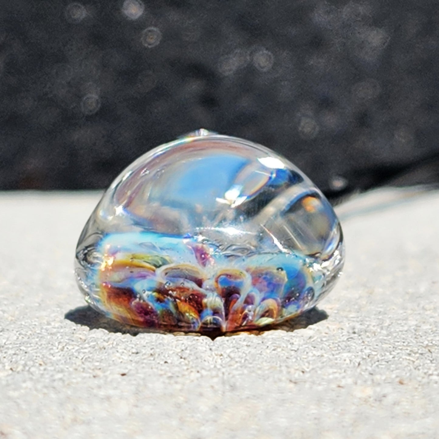 Side view of UV Glow Glass Pendant showing dome shape and vibrant internal flower design. Blown glass jewelry with colorful detail.
