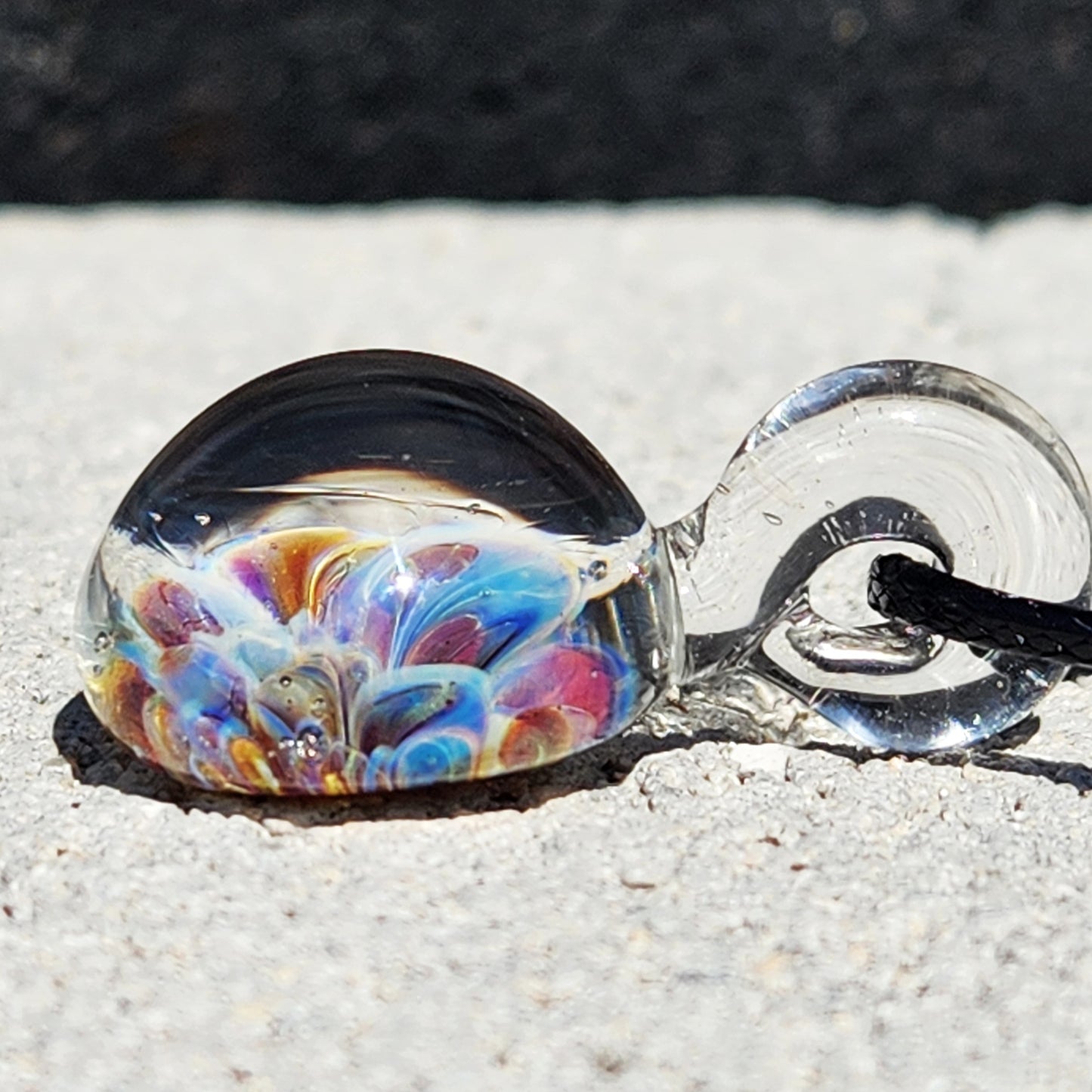 Side profile of UV Glow Glass Pendant showing colorful internal flower and clear loop. Lightweight blown glass charm for unique accessories.