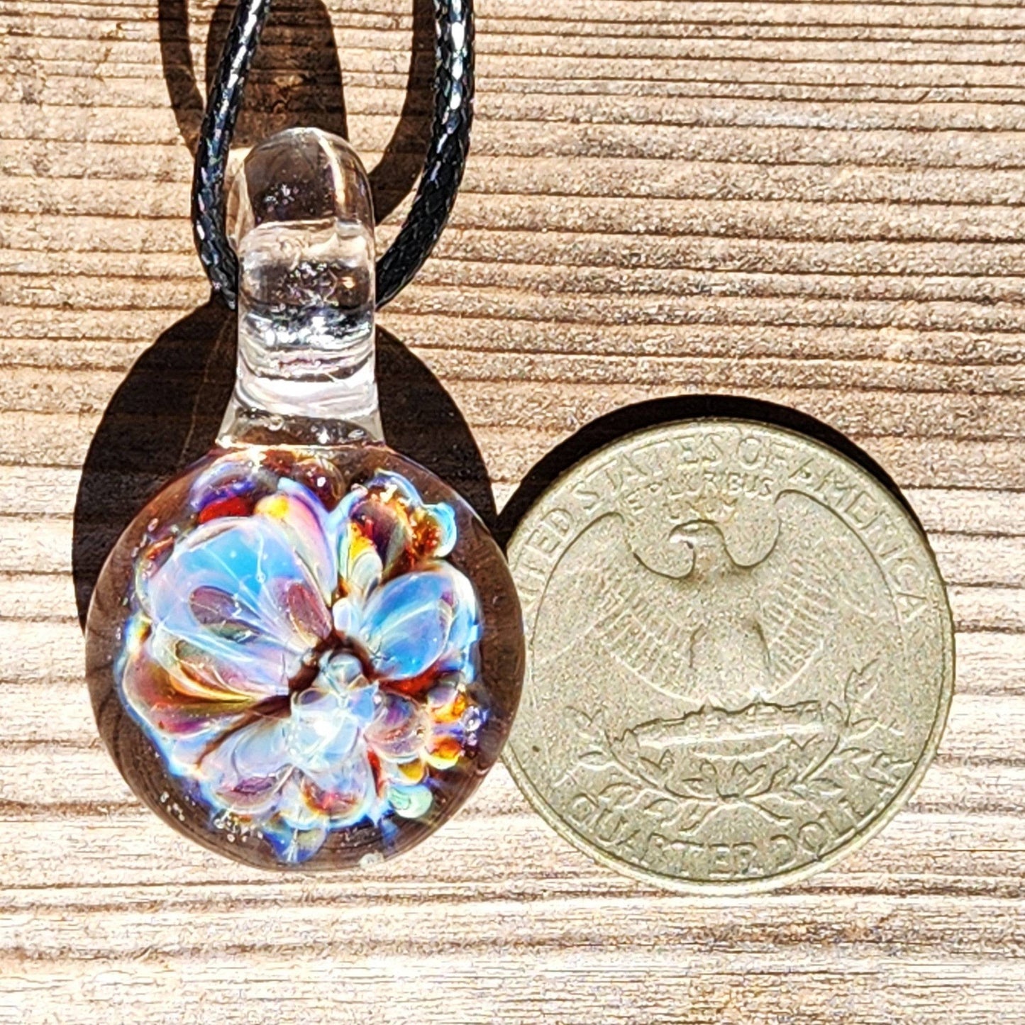 UV Glow Glass Pendant next to a U.S. quarter for size comparison, showing detailed flower design. Small handmade blown glass charm necklace.