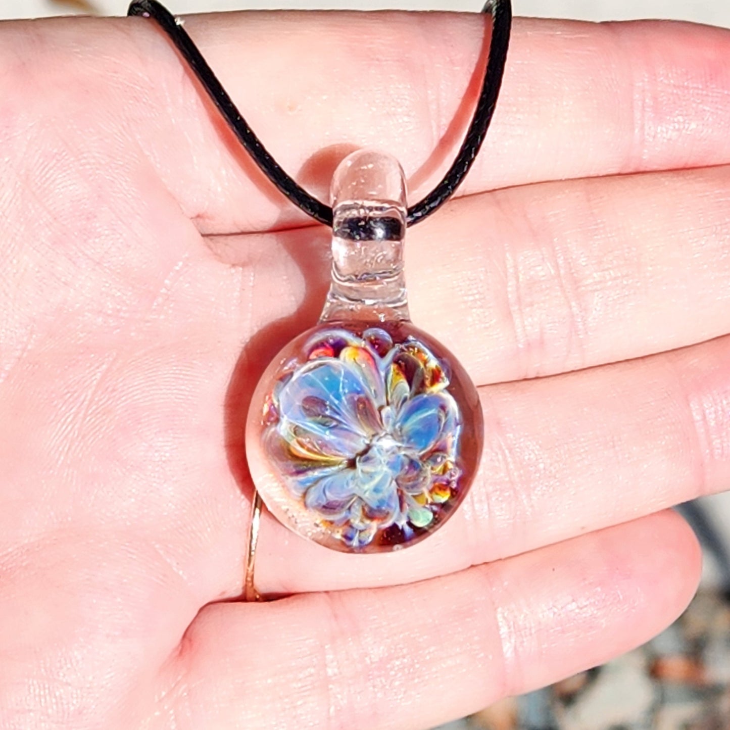 UV Glow Glass Pendant held in hand, showing size and intricate flower design. Handmade blown glass necklace ideal for gifts and festivals.