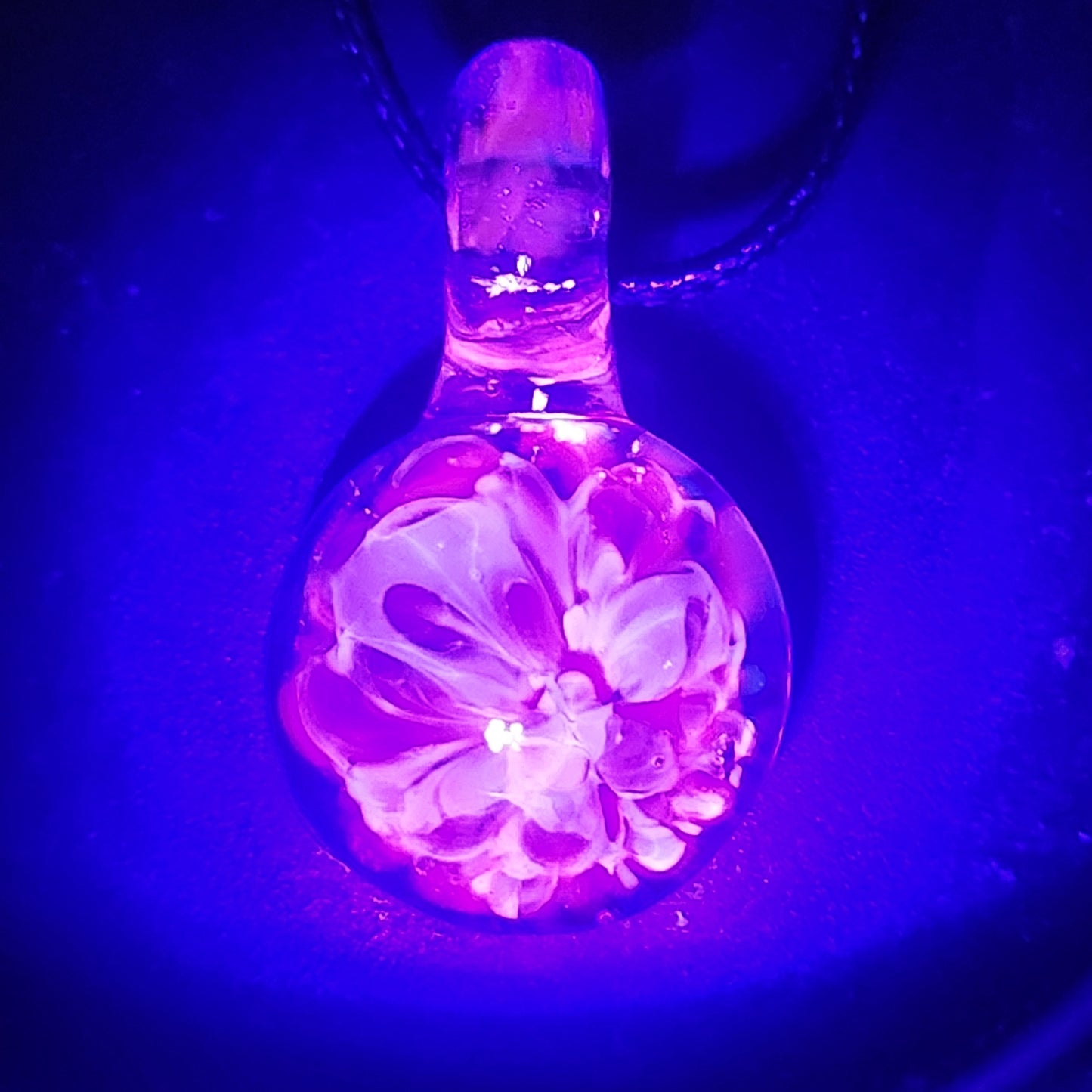 UV Glow Glass Pendant glowing pink under blacklight, showcasing handmade blown glass flower design. Ideal for festivals and unique jewelry lovers.