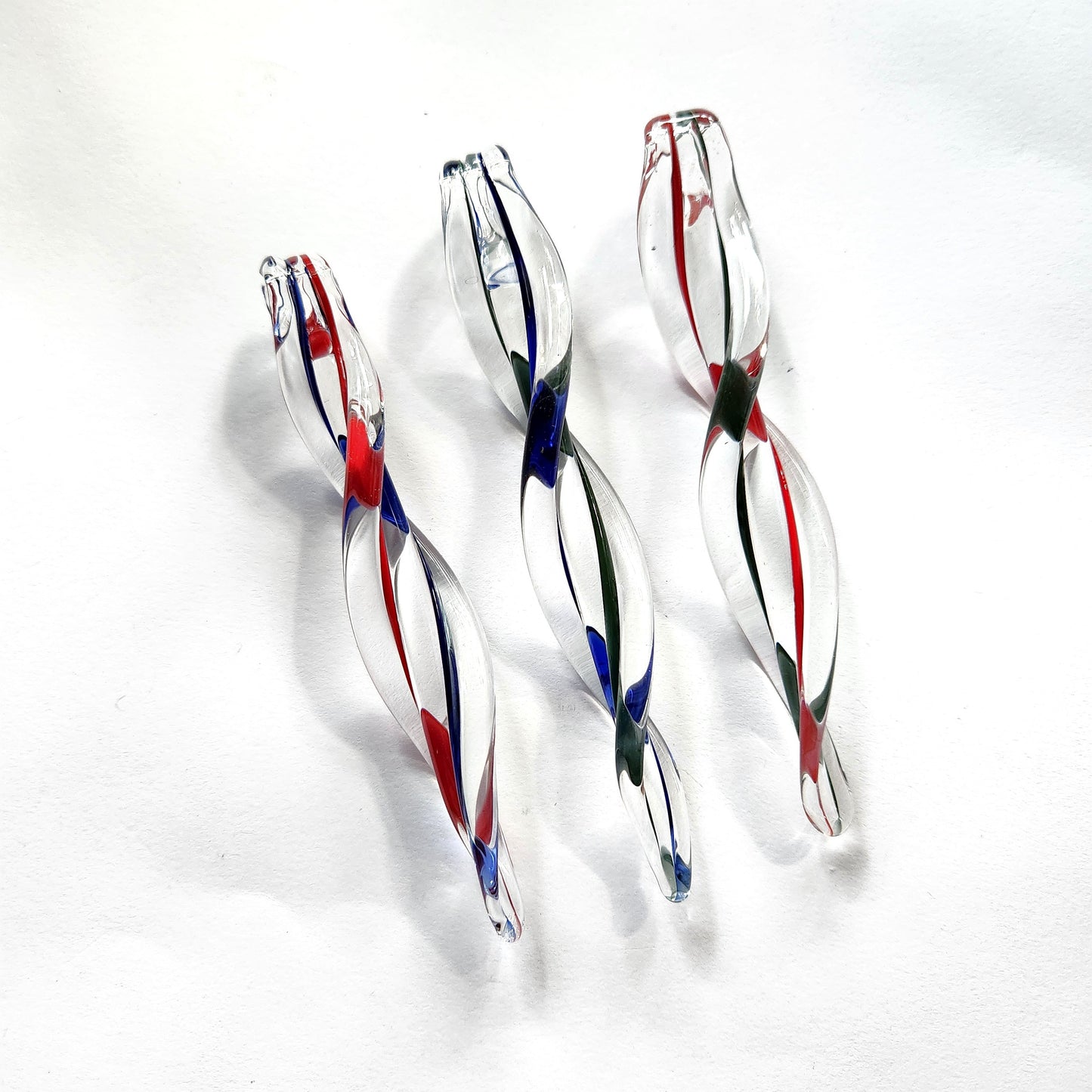 Three handblown glass icicle ornaments with red, green, and blue swirls on white background. Perfect for festive holiday decoration.