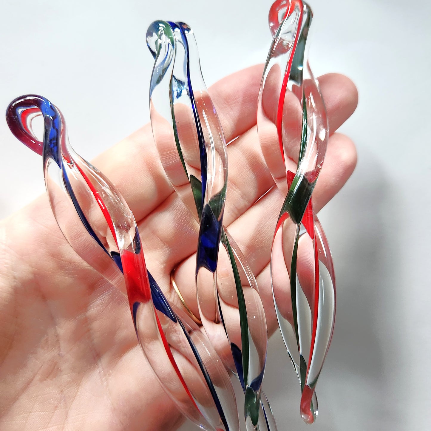 Close-up of 3 handmade glass icicle ornaments held in hand, showcasing red, green, and blue swirls. Unique holiday gift idea.